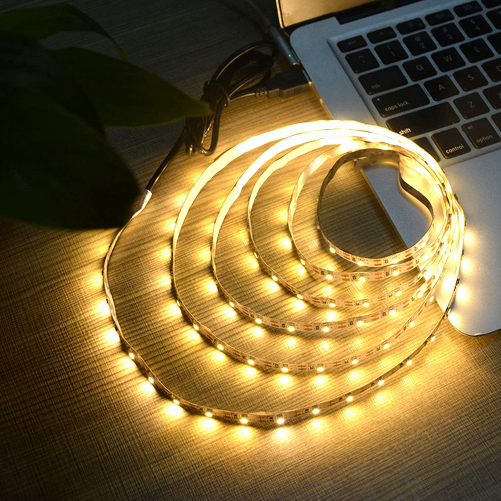 Ein leuchtender LED-Streifen, der auf einer Holzoberfläche aufgerollt ist, neben einer Laptop-Tastatur. Der Streifen beleuchtet die Szene.