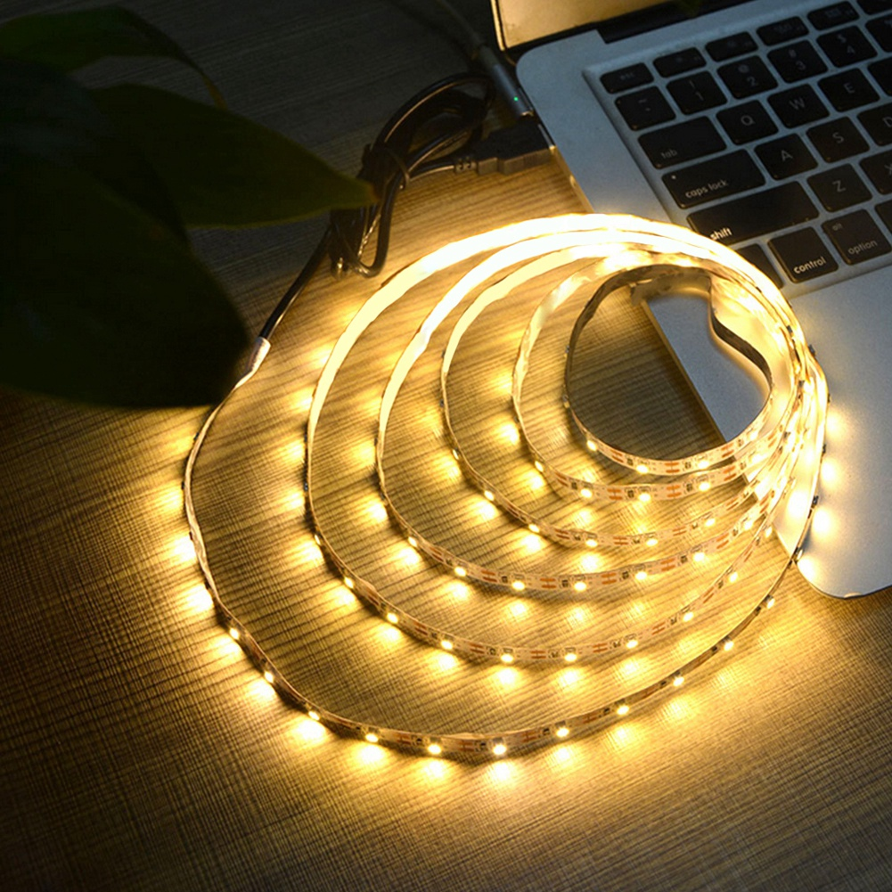 Ein leuchtender LED-Streifen, der auf einer Holzoberfläche aufgerollt ist, neben einem Laptop. Der Streifen ist mit einer Stromquelle verbunden.