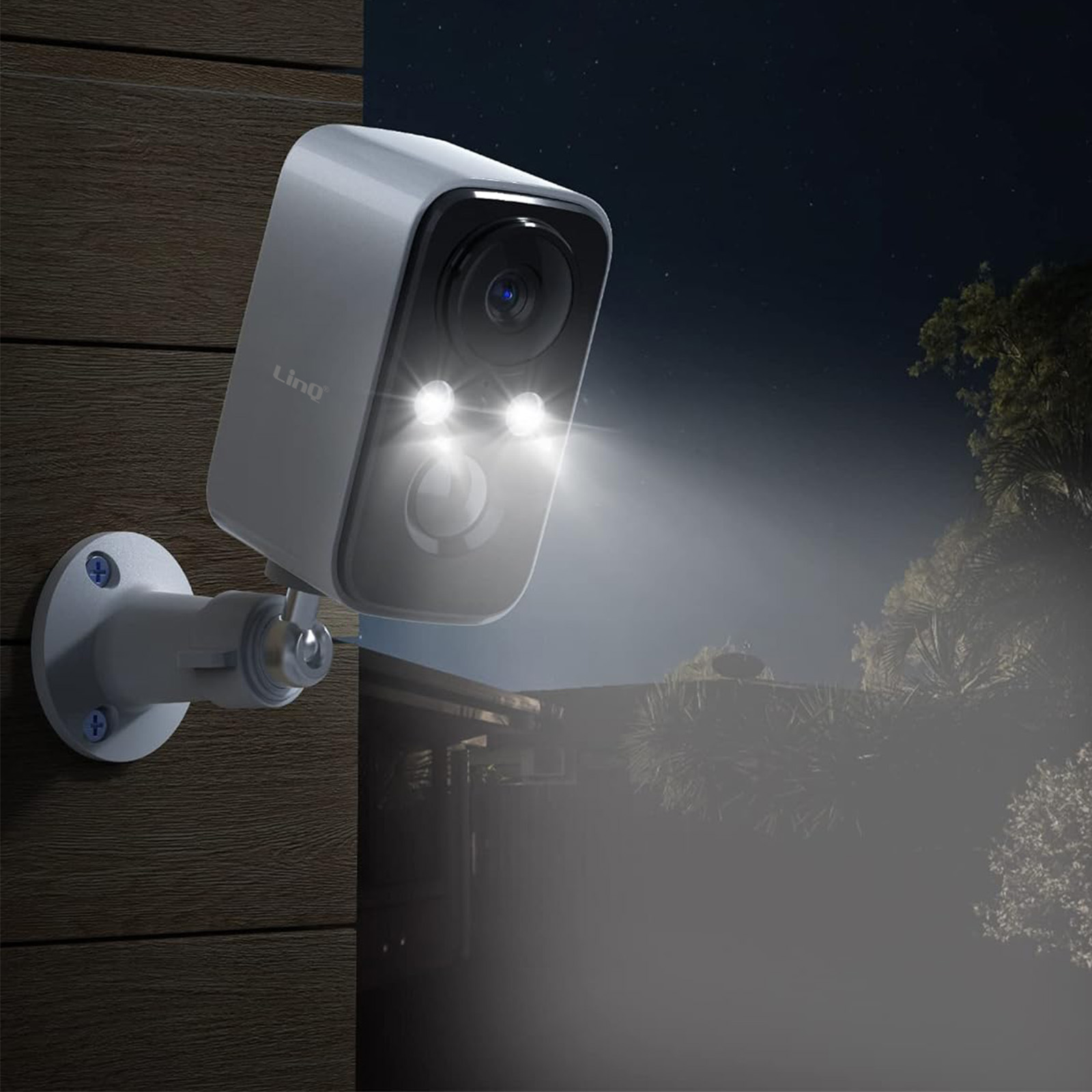 Una cámara de seguridad con luces brillantes está montada en una pared de madera por la noche. El fondo muestra una casa y árboles.
