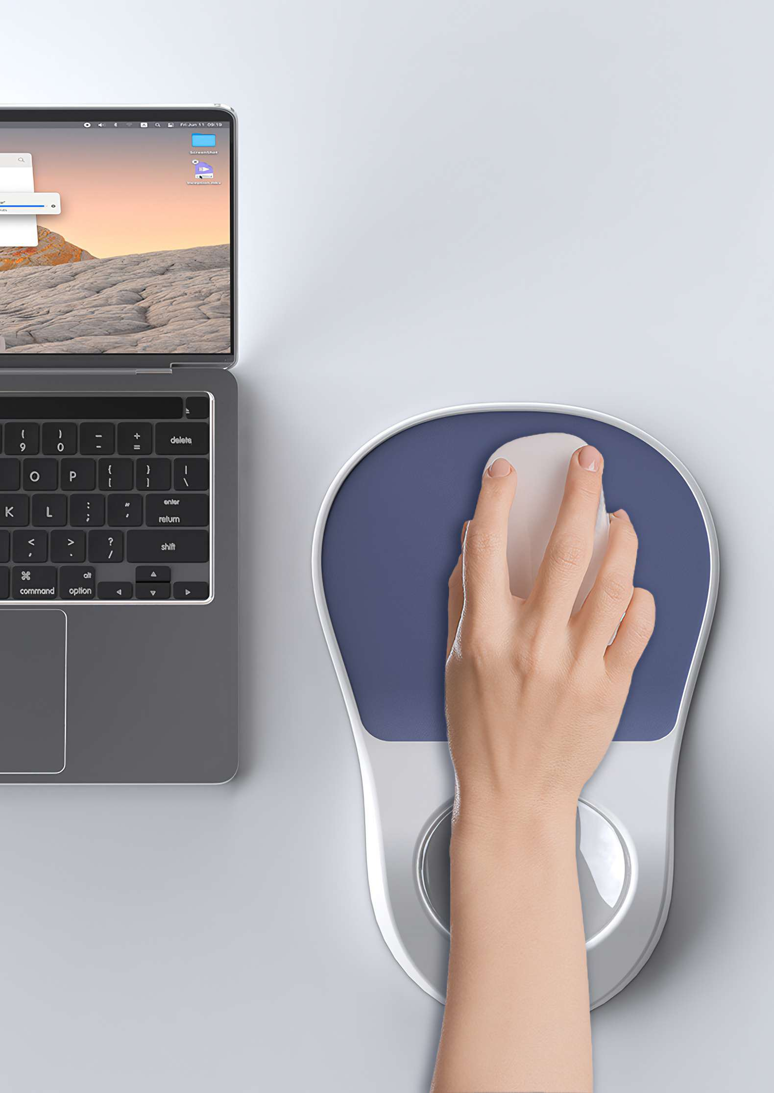 Eine Hand benutzt eine weiße Maus auf einem blauen Mauspads neben einem Laptop auf einer weißen Oberfläche.