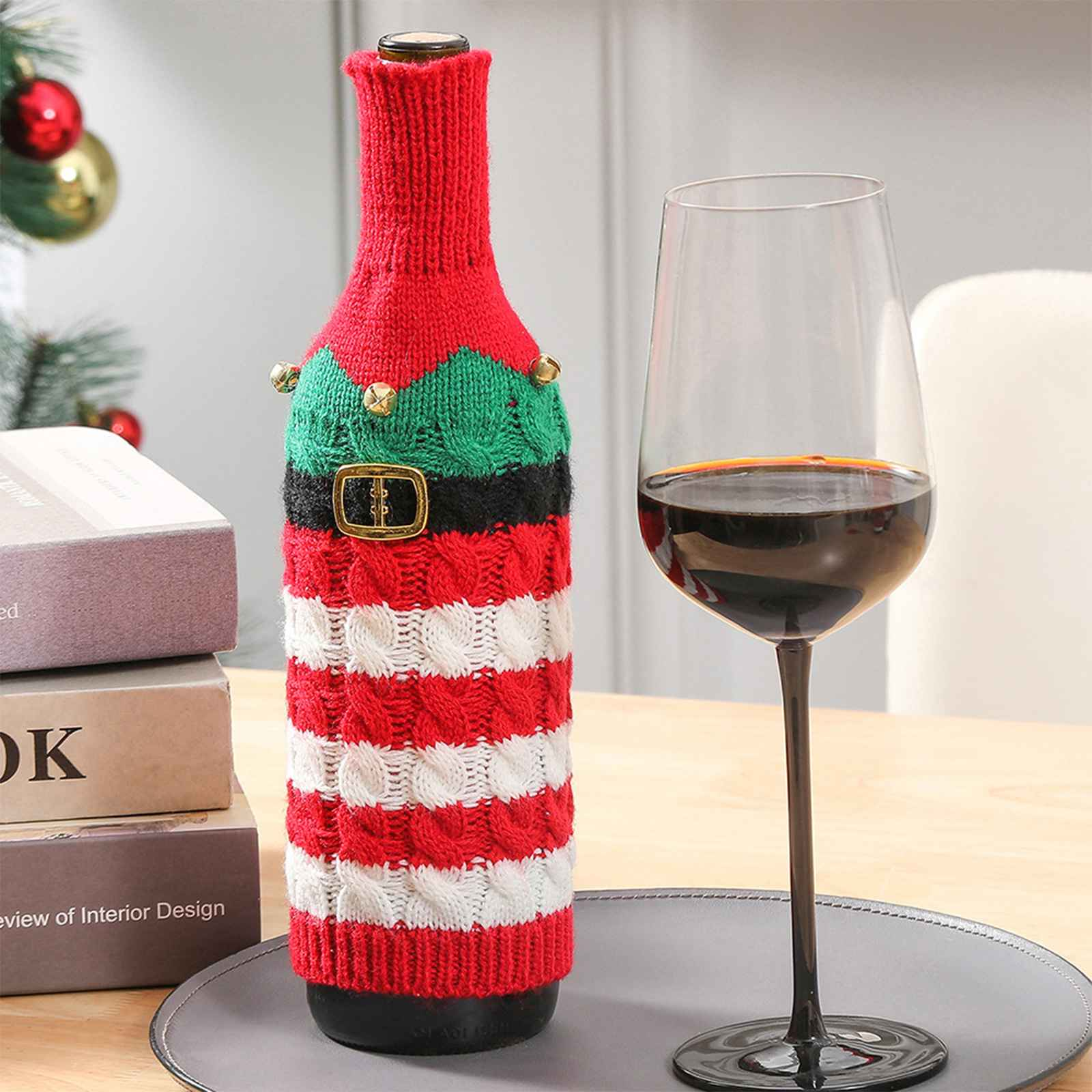 Eine Weinflasche in einem Weihnachtspullover und ein Weinglas mit Rotwein auf einem Tisch.