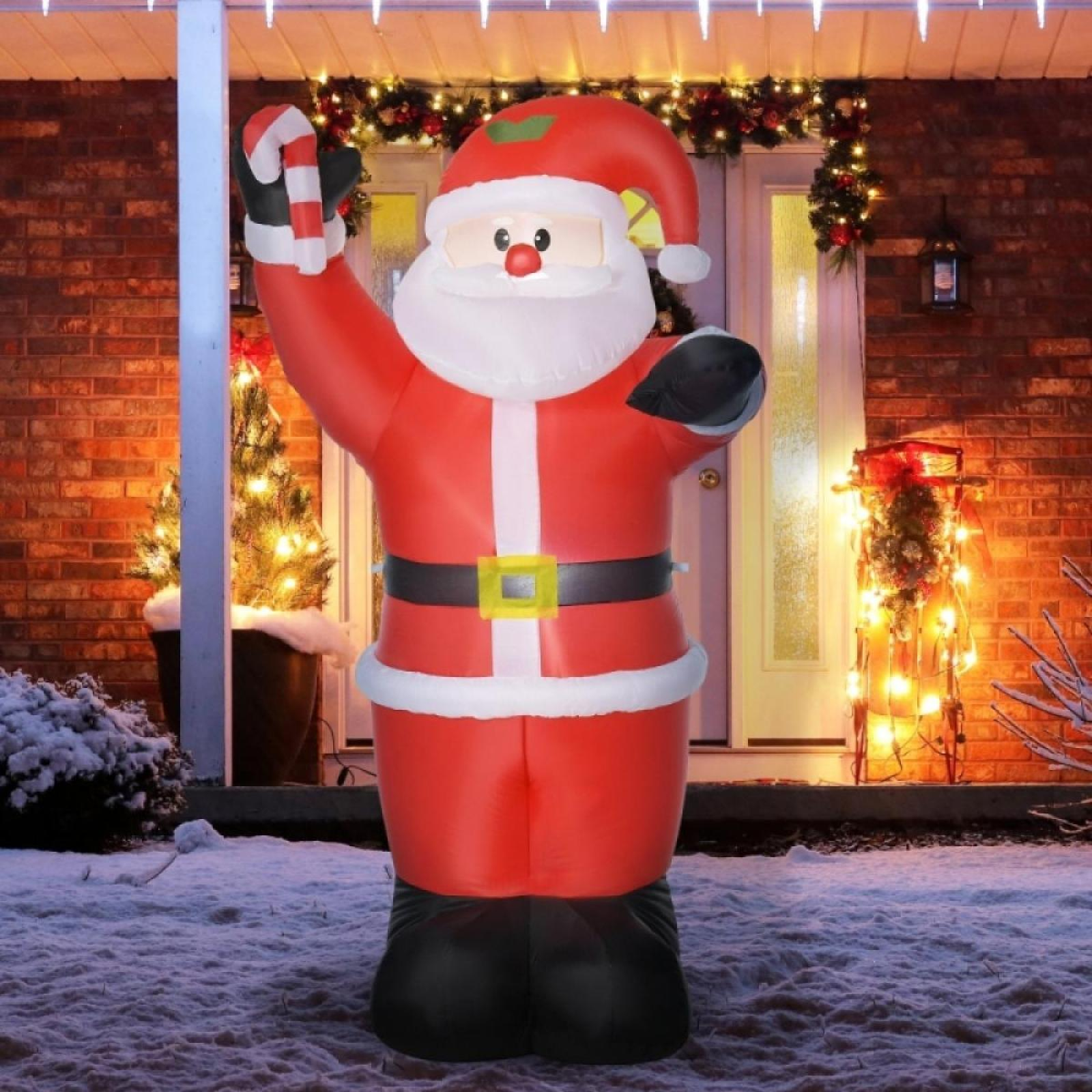 Aufblasbarer Weihnachtsmann mit Zuckerstange im Schnee. Weihnachtslichter und Dekorationen schmücken den Eingang eines Hauses.