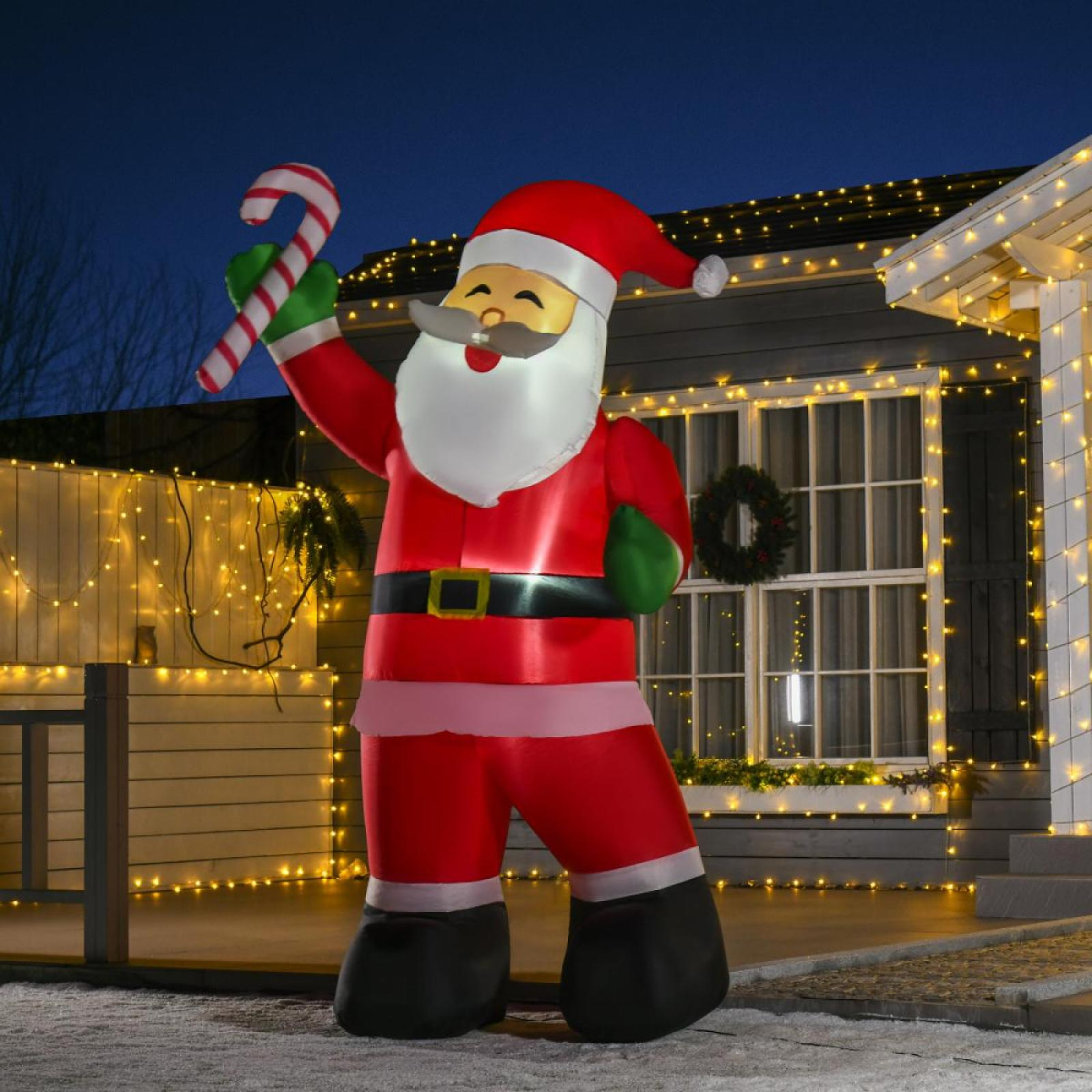Ein aufblasbarer Weihnachtsmann hält eine Zuckerstange. Er steht vor einem mit Weihnachtsbeleuchtung geschmückten Haus bei Nacht.