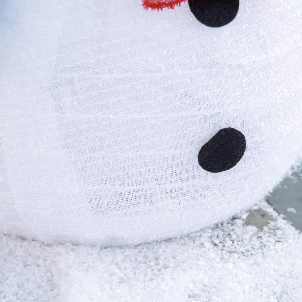 Nahaufnahme eines Schneemannkopfes. Schwarze Augen und ein kleiner roter Schal sind sichtbar. Der Schneemann steht auf einer schneebedeckten Oberfläche.