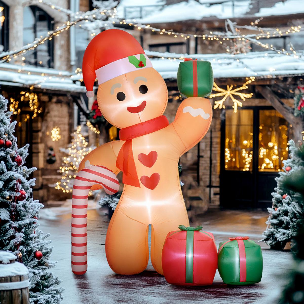Aufblasbarer Lebkuchenmann mit rotem Hut und Schal, hält ein Geschenk. Zwei Geschenke am Boden. Schnee und Weihnachtsbeleuchtung im Hintergrund.