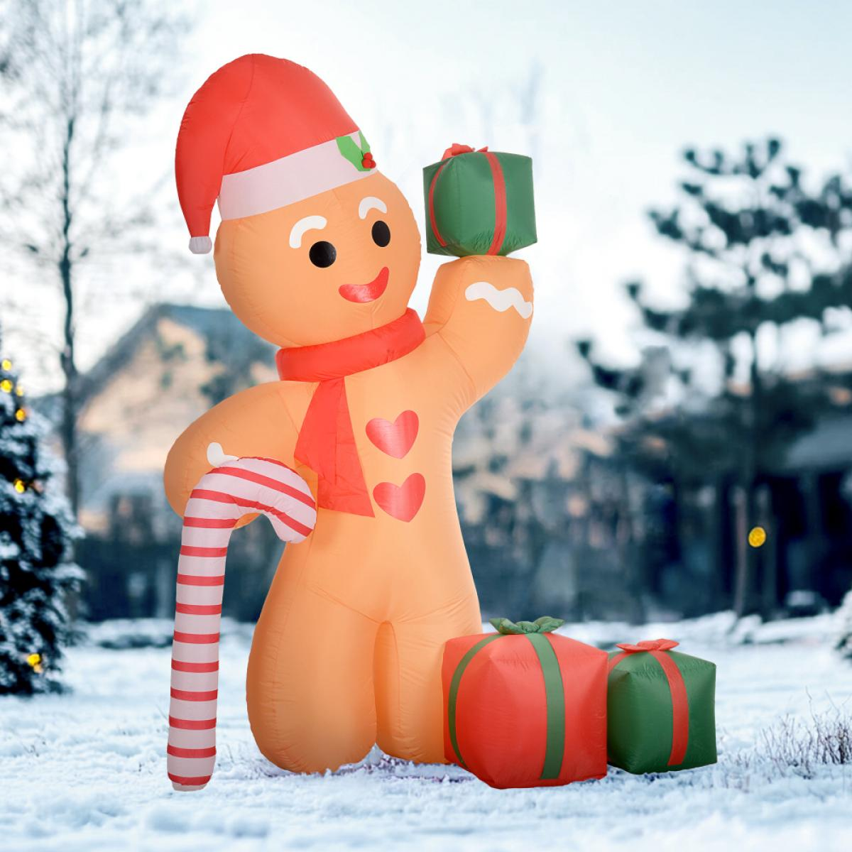 Aufblasbarer Lebkuchenmann mit Zuckerstange, hält ein Geschenk. Weihnachtsdekoration, Schnee im Hintergrund.