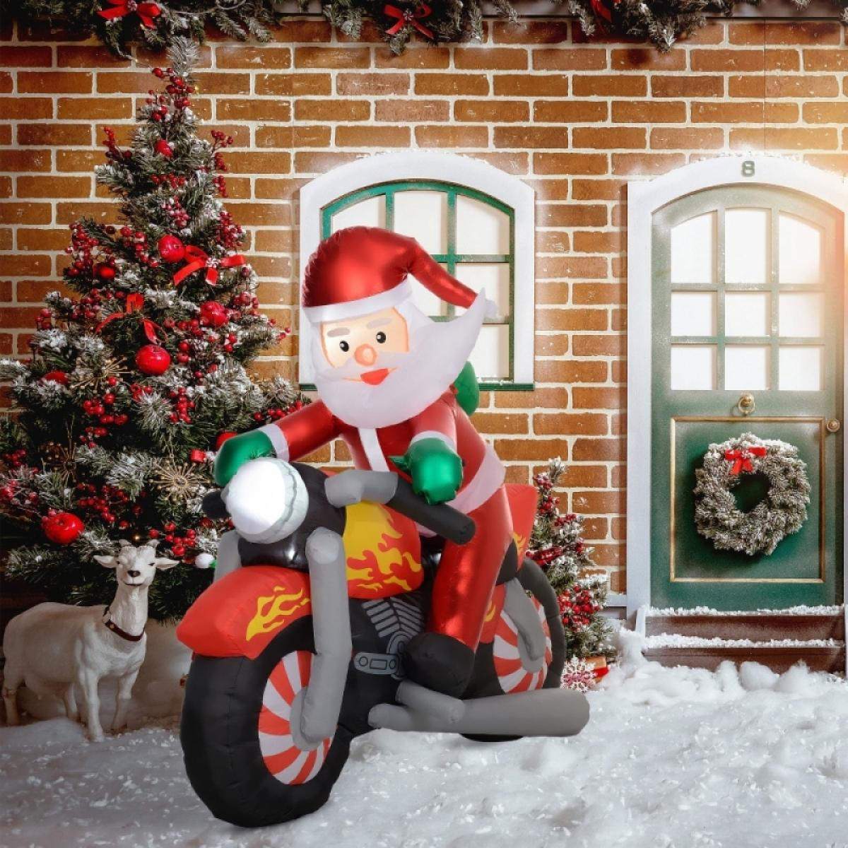 Aufblasbarer Weihnachtsmann auf rotem Motorrad mit Flammen, vor einem Backsteinhaus und Weihnachtsbaum.