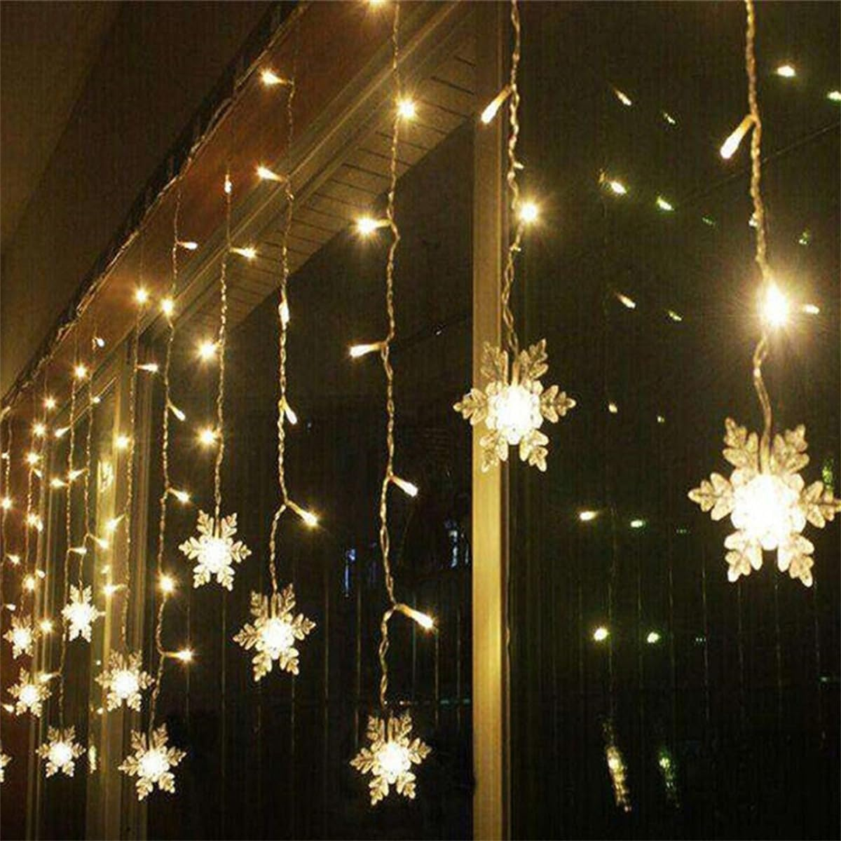 Lichterketten mit Schneeflocken-Dekorationen hängen vor einem Fenster und erzeugen einen warmen, festlichen Schein.
