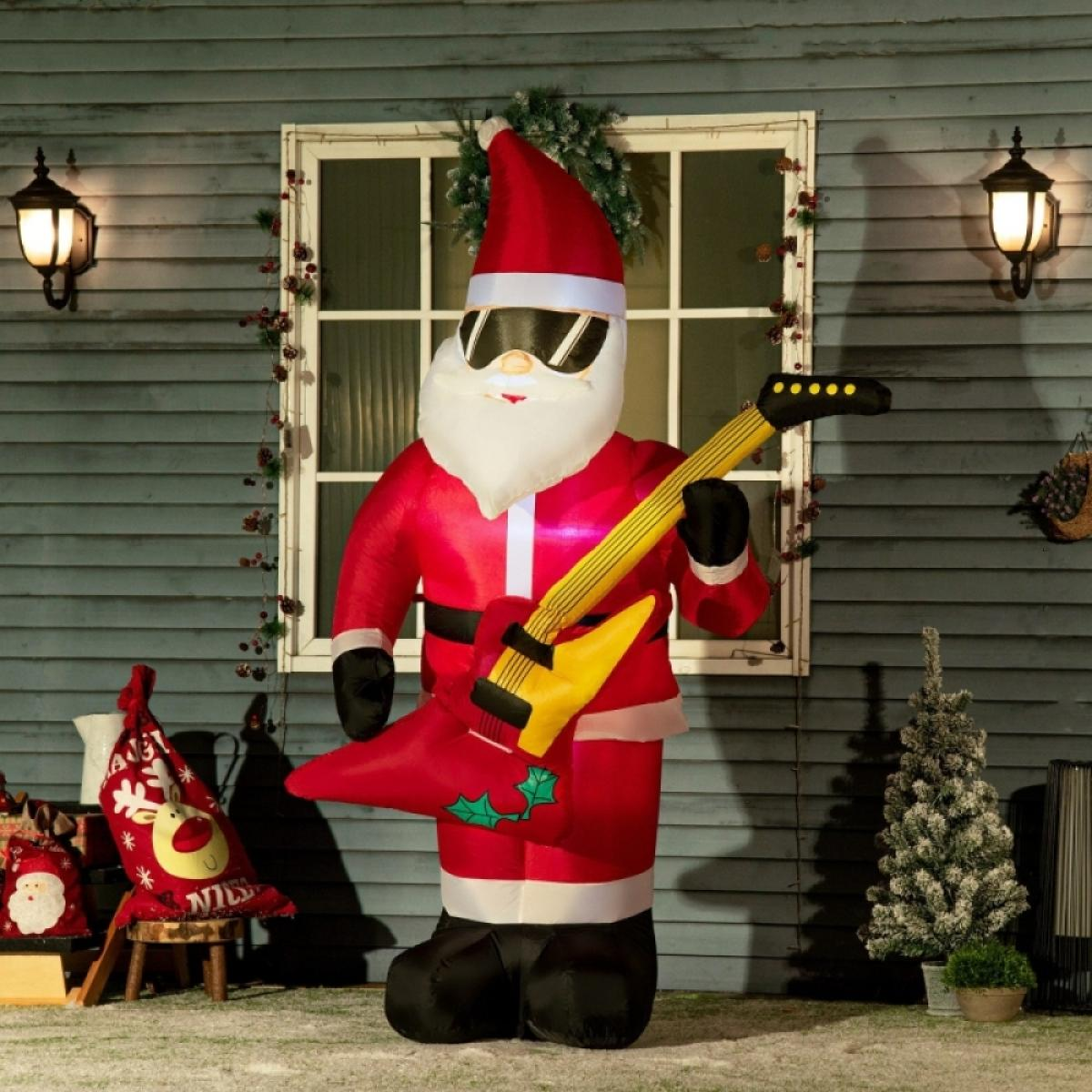 Aufblasbarer Weihnachtsmann mit Sonnenbrille spielt eine gelbe Gitarre. Er steht vor einem blauen Haus mit Weihnachtsdekorationen.