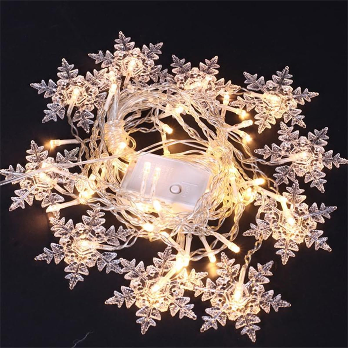 Eine Lichterkette mit Schneeflocken leuchtet vor einem schwarzen Hintergrund. In der Mitte befindet sich ein Akku.
