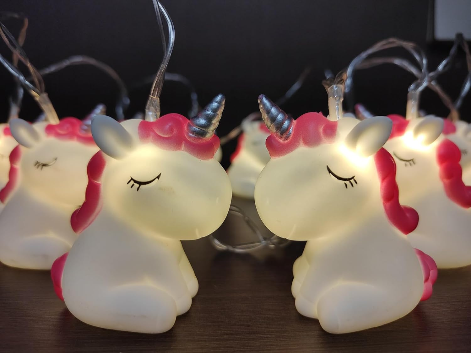 Nahaufnahme von Einhorn-Lichterketten. Weiße Körper mit rosa Mähnen, silbernen Hörnern und geschlossenen Augen, die sanft leuchten.