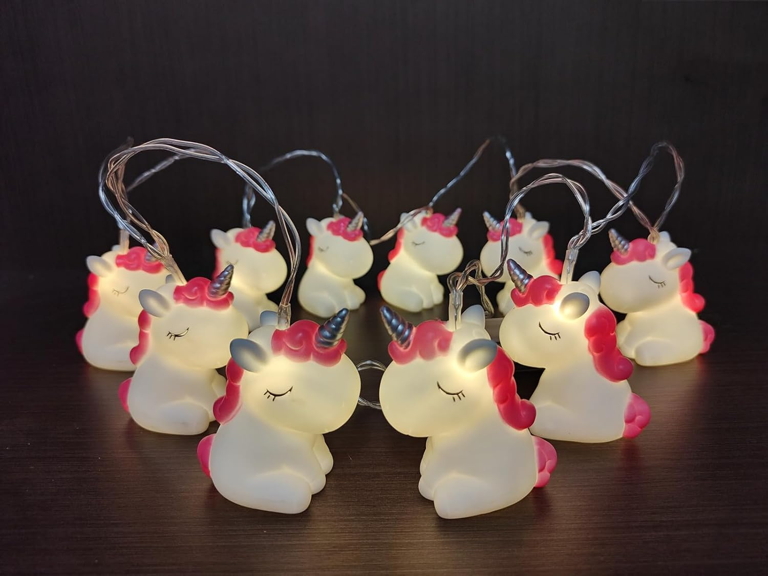Lichterkette mit leuchtenden Einhörnern. Jedes hat eine rosa Mähne und ein Horn, einen weißen Körper und geschlossene Augen.