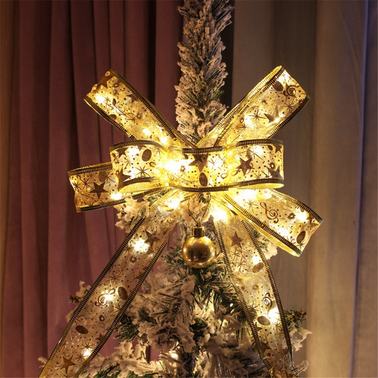 Eine Christbaumschleife aus goldenem Band mit Sternen und Lichtern. Darunter hängt ein goldener Schmuck.