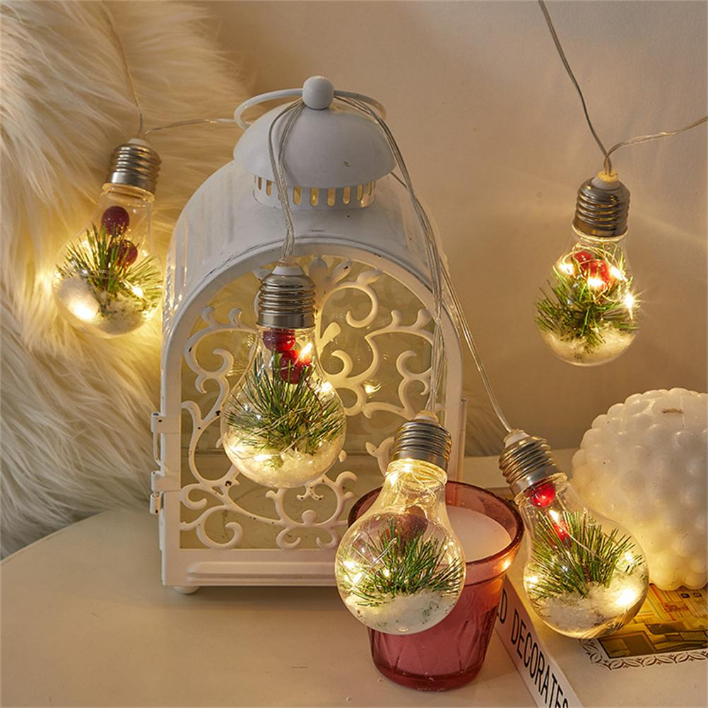 Lichterkette mit Grün, Beeren und Schnee. Im Hintergrund eine weiße Laterne.
