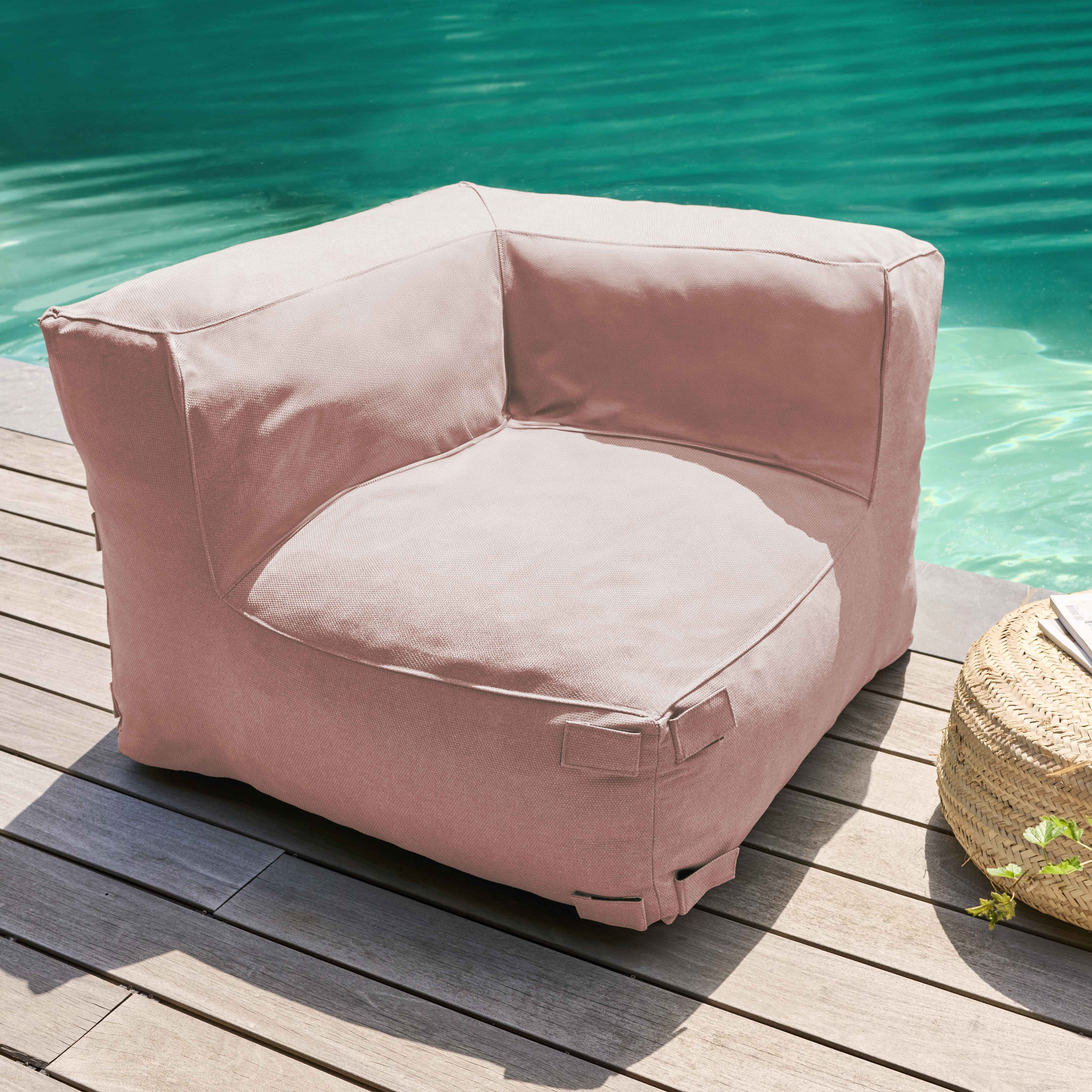 Ein rosa Ecksofa steht auf Holzterrassen neben einem Pool. Rechts sind ein geflochtener Korb und Grün.