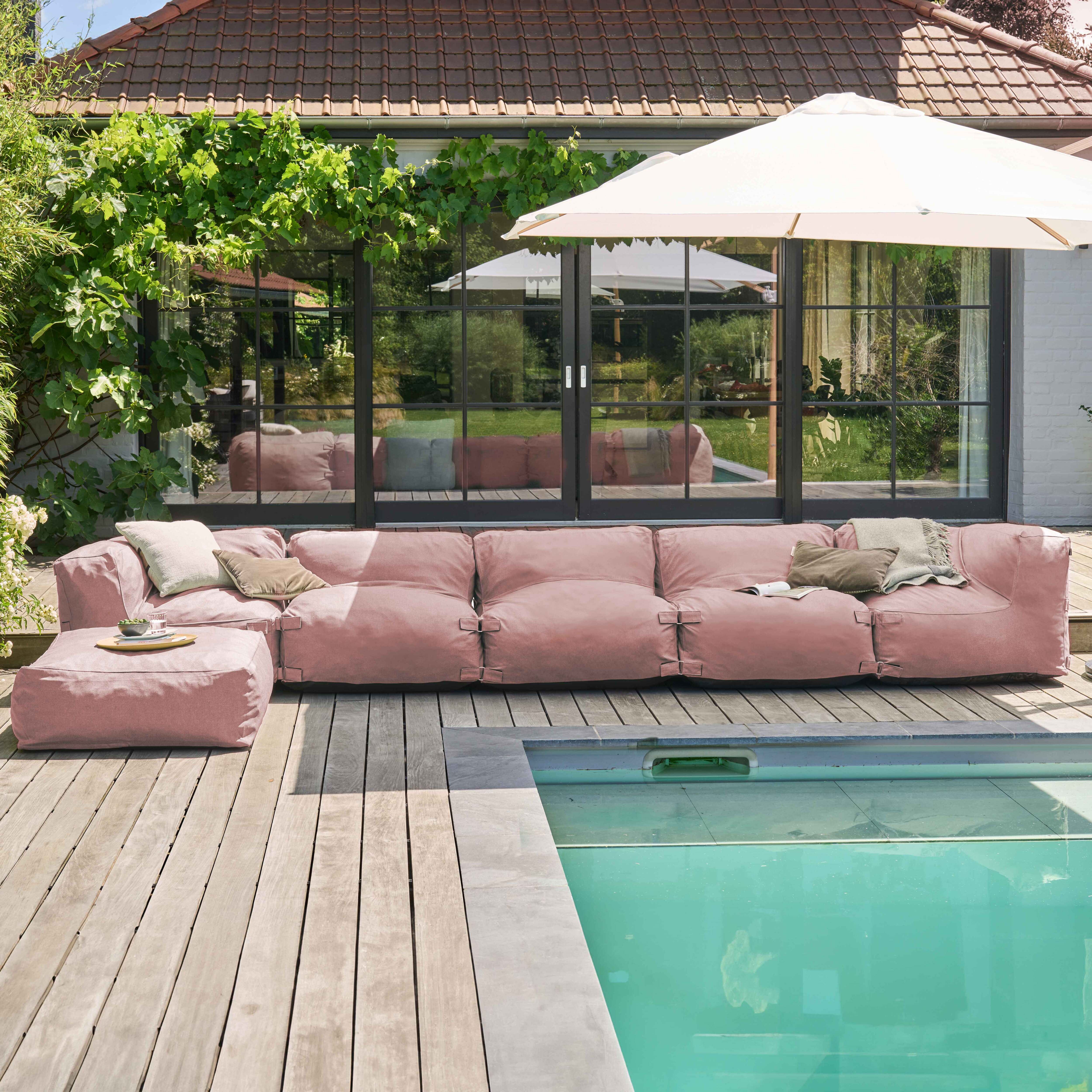 Moderne Außenszene mit rosa Sofa, Pool und weißem Sonnenschirm. Im Hintergrund ein Haus mit Glastüren.