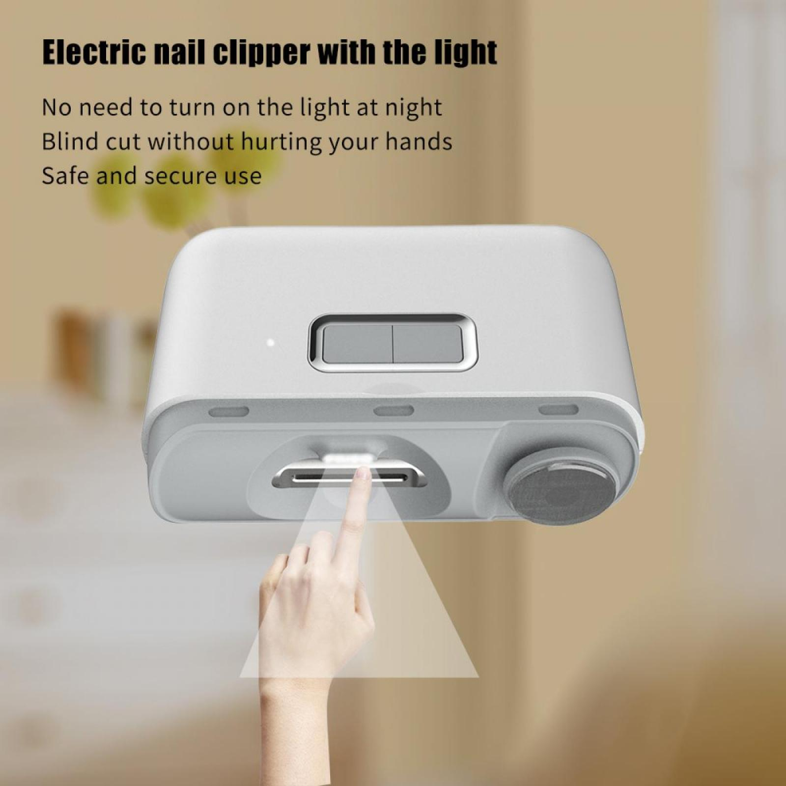 Elektrischer Nagelknipser mit Licht. Ein Finger drückt auf eine Taste. Weißes Gerät, beiger Hintergrund.