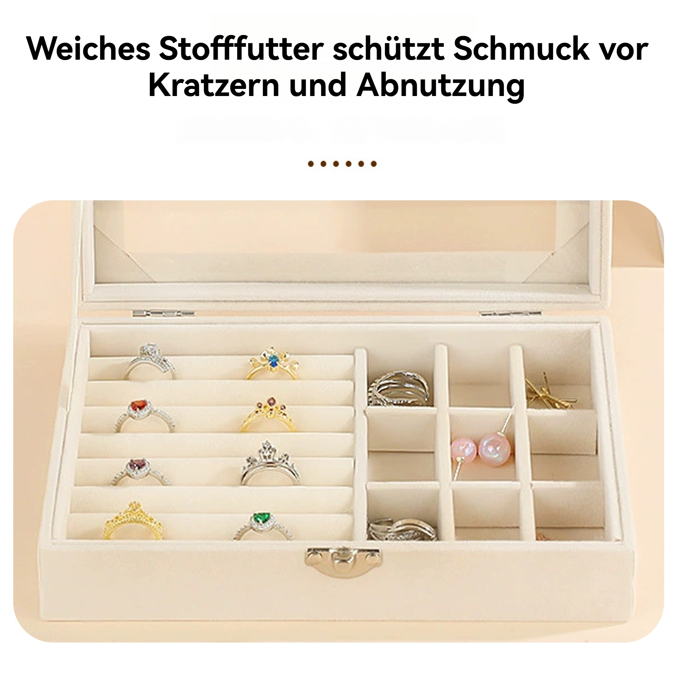 Geöffnete Schmuckschatulle mit Ringen und Ohrringen. Beige Innenausstattung, Glasdeckel, Text oben. Ringe mit Edelsteinen.