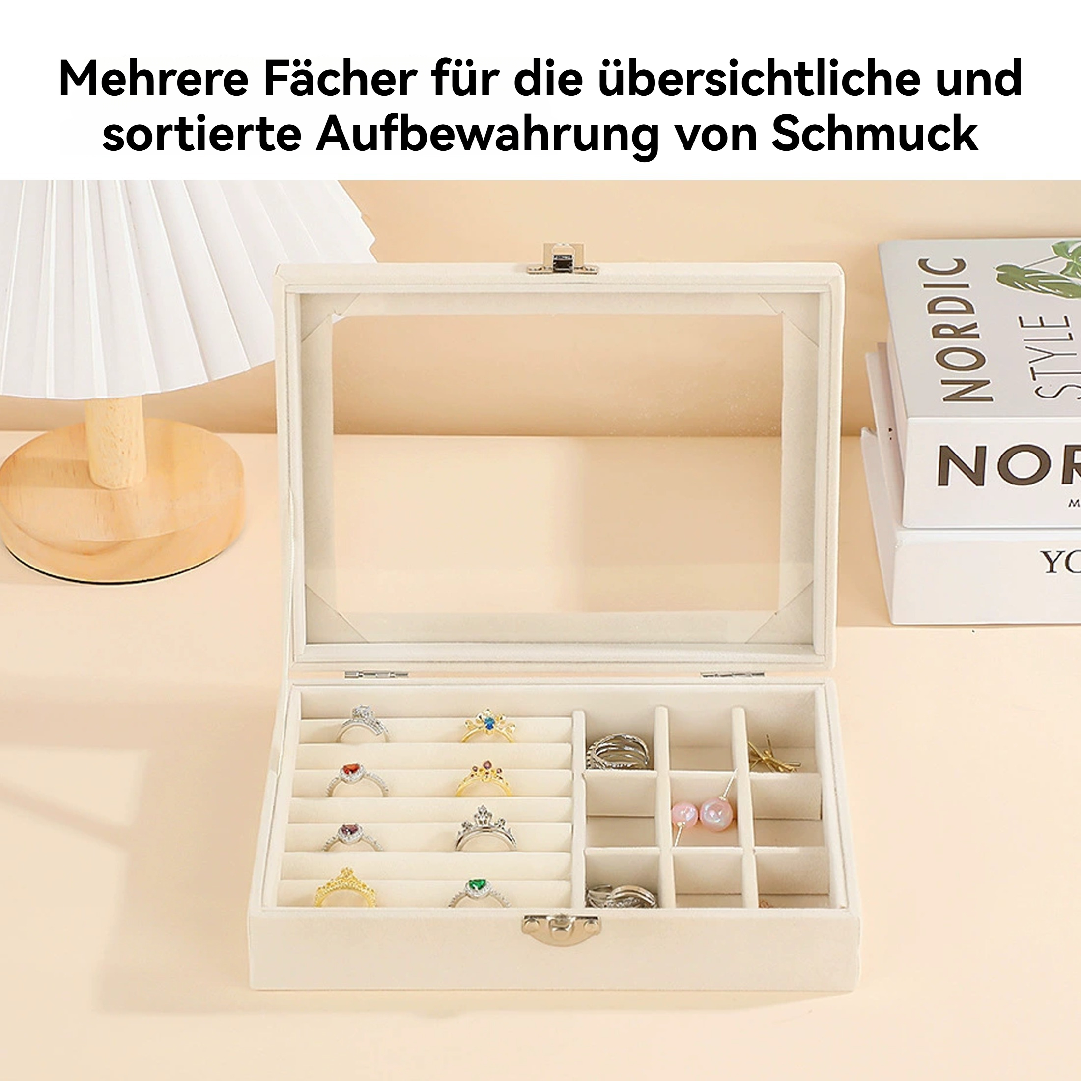 Eine Schmuckschatulle mit Ringen, Ohrringen und einer Lampe im Hintergrund. Bücher sind rechts.