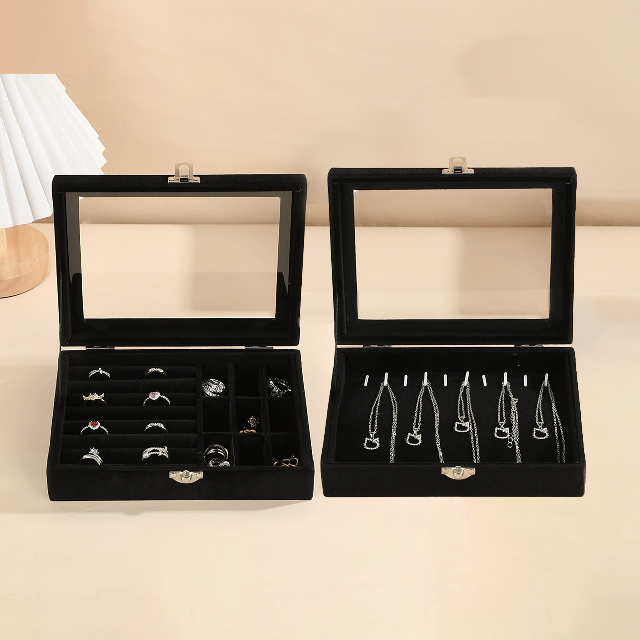 Zwei offene schwarze Schmuckkästchen mit Glasdeckeln. Die linke Box enthält Ringe, die rechte Halsketten.