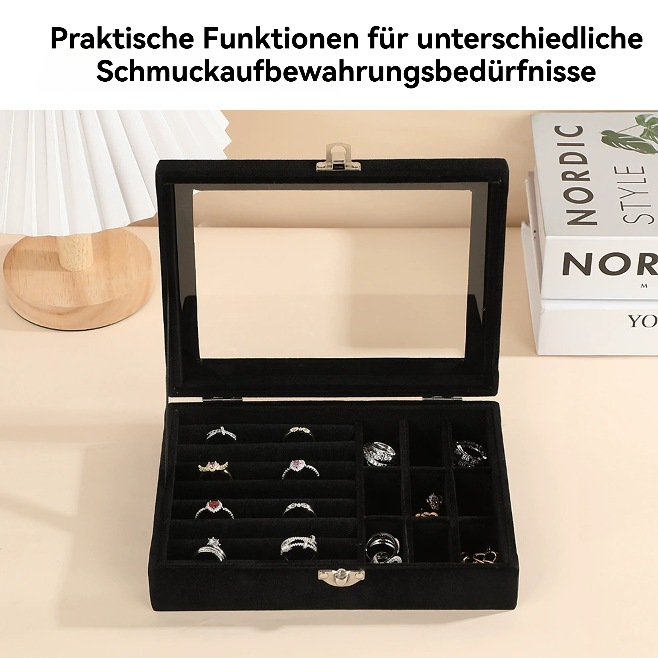Eine schwarze Schmuckschatulle mit Ringen, eine Lampe und Bücher auf heller Oberfläche.