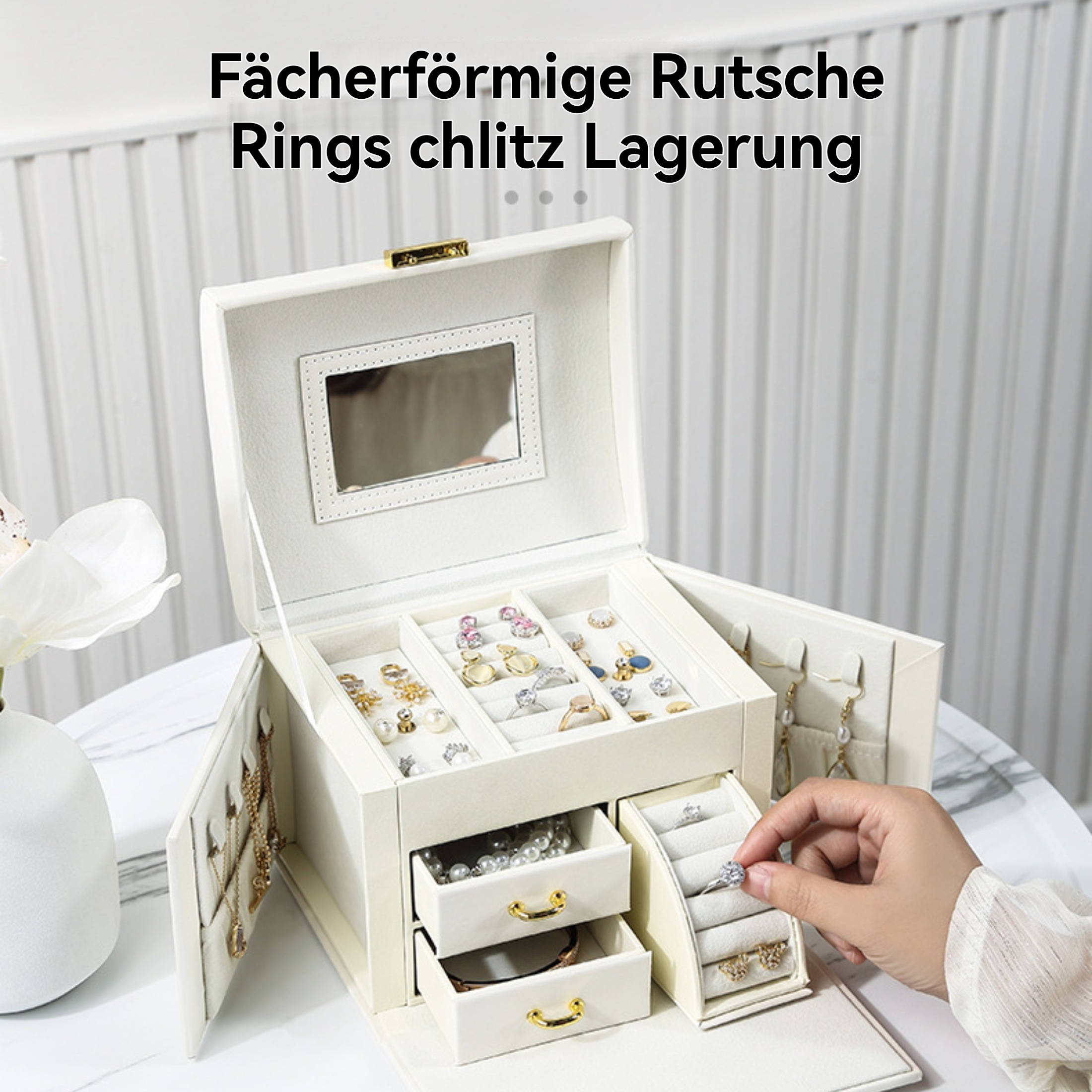 Eine cremefarbene Schmuckschatulle ist geöffnet und zeigt Ringe und Halsketten. Eine Hand hält einen Ring. Im Hintergrund ist eine weiße Wand.