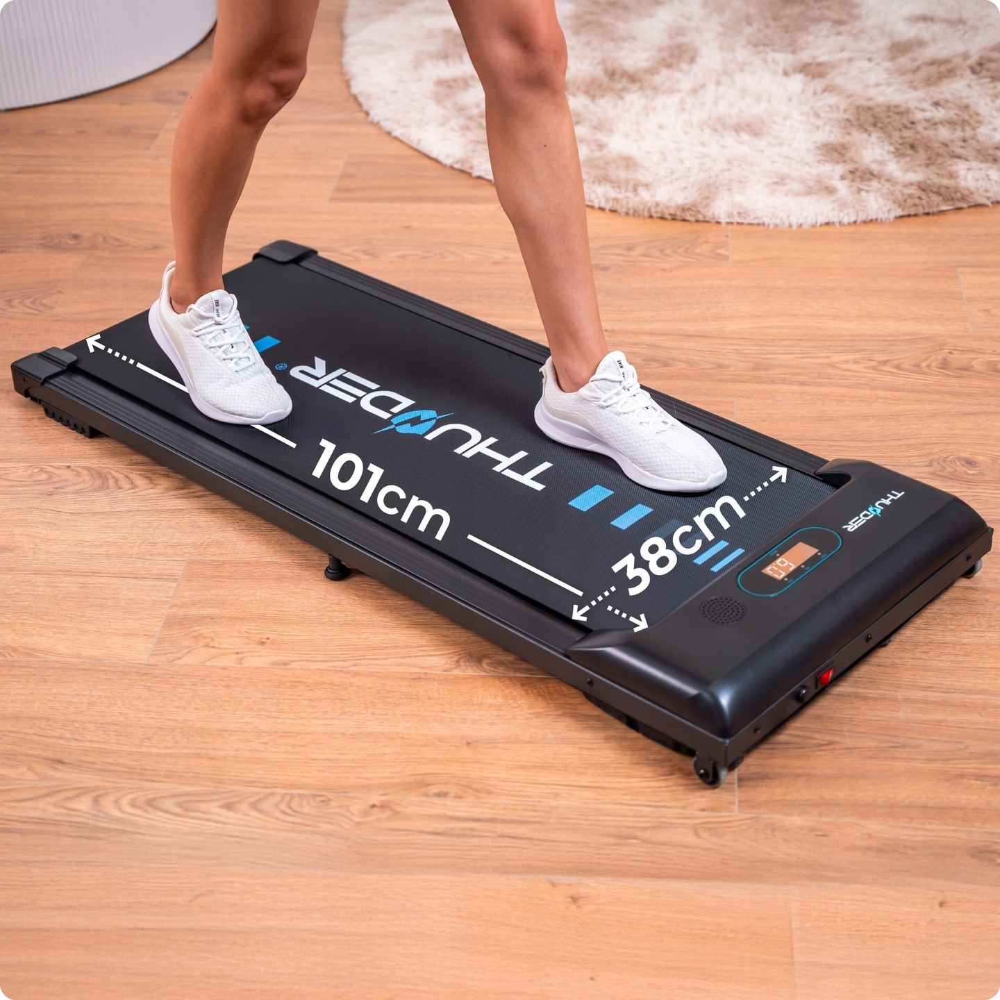 Osoba idzie po czarnej bieżni w białych butach. Wyświetlane są wymiary. Podłoga jest drewniana, w tle dywan.