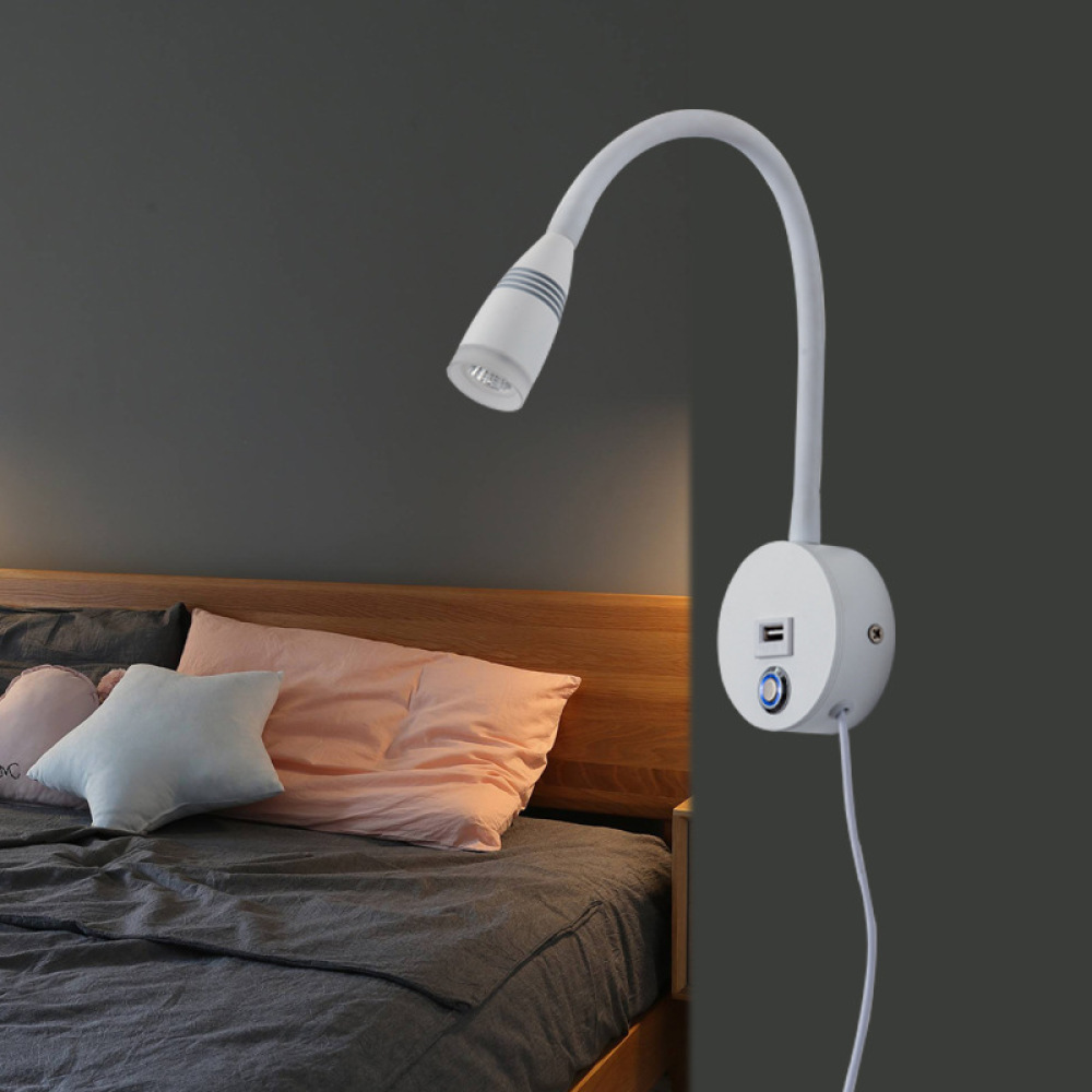 Eine weiße, an der Wand montierte Leselampe mit flexiblem Hals befindet sich neben einem Bett mit Kissen. Der Hintergrund ist eine dunkelgraue Wand.