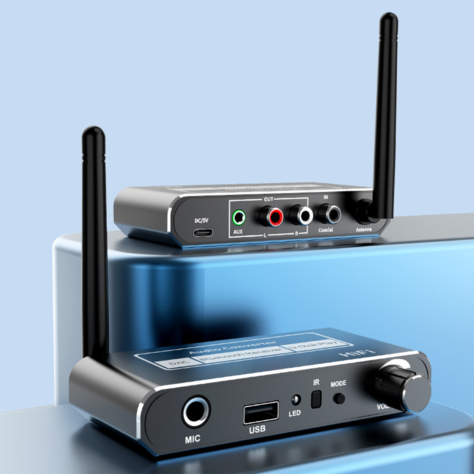 Zwei schwarze Audio-Konverter mit Antennen auf einer blauen Oberfläche. Einer liegt auf dem anderen. Beschriftungen: MIC, USB, AUX, Koaxial.