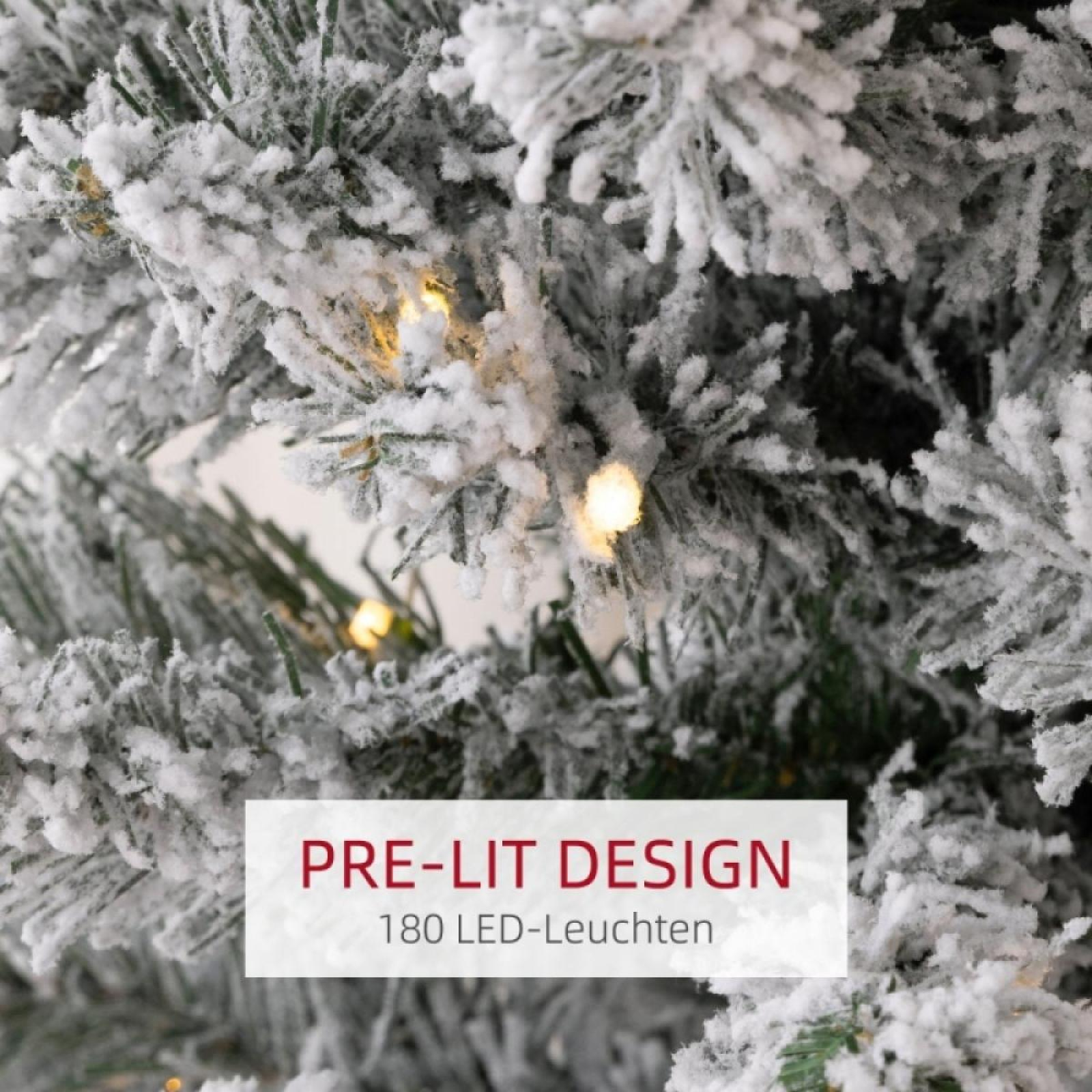 Nahaufnahme eines schneebedeckten Weihnachtsbaums mit vorbeleuchteten warmen Lichtern. Ein Banner zeigt 'PRE-LIT DESIGN' und '180 LED-Leuchten'.