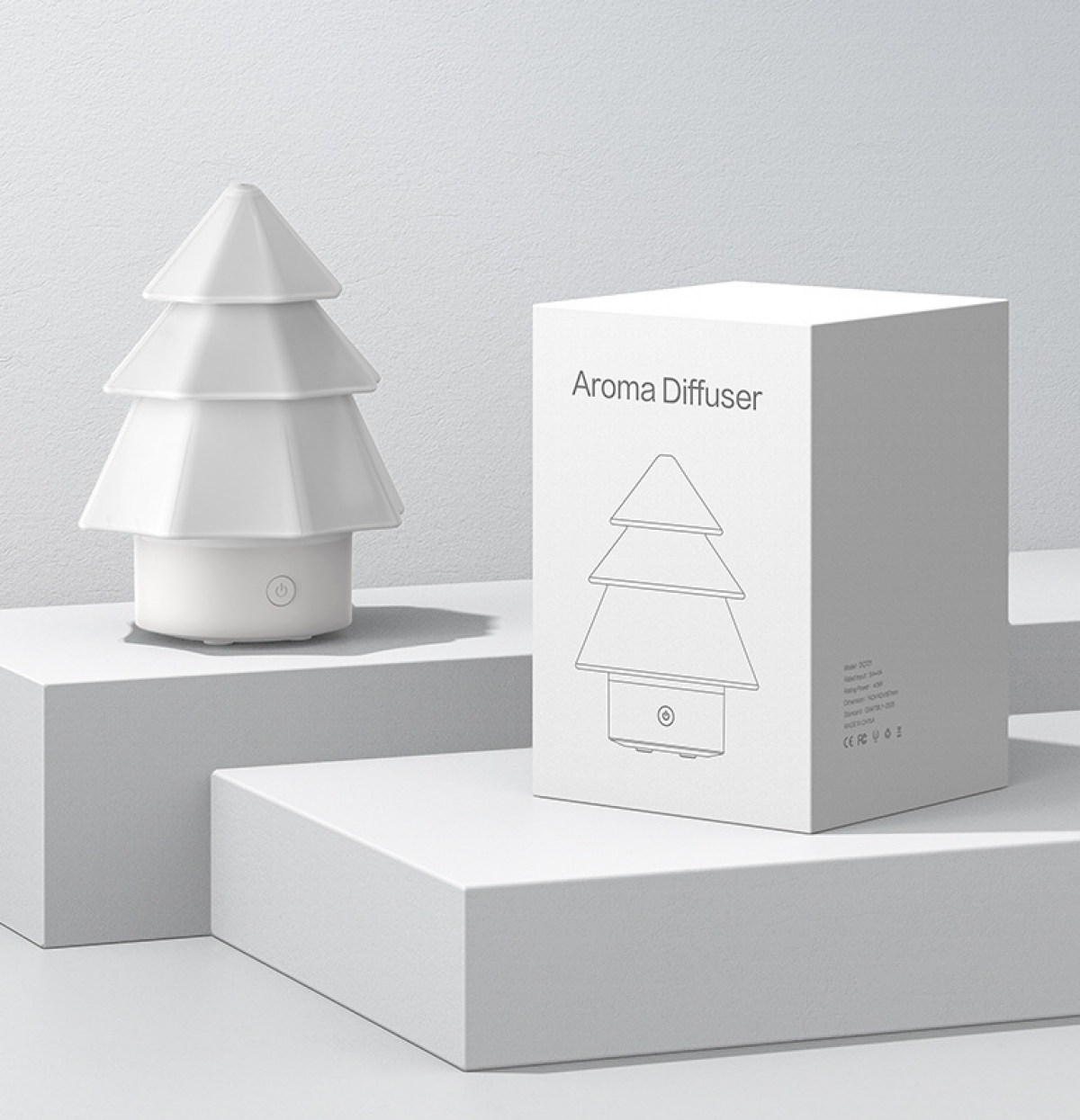 Ein weißer Aroma-Diffusor in Form eines Weihnachtsbaums und eine Schachtel mit dem gleichen Design, platziert auf weißen Blöcken.