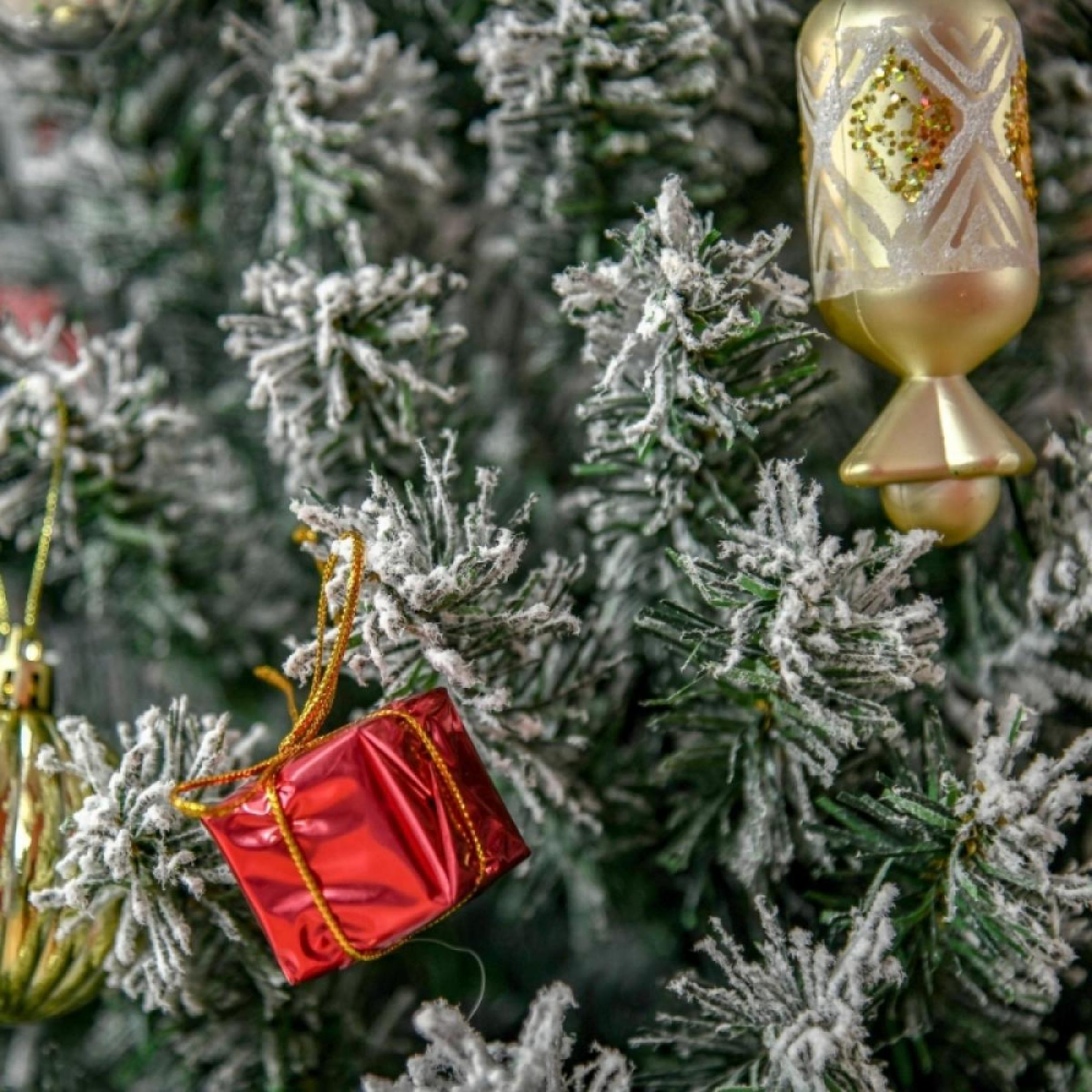 Weihnachtsbaum mit Verzierungen. Eine rote Geschenkbox und goldene Dekorationen hängen zwischen schneebedeckten Ästen.
