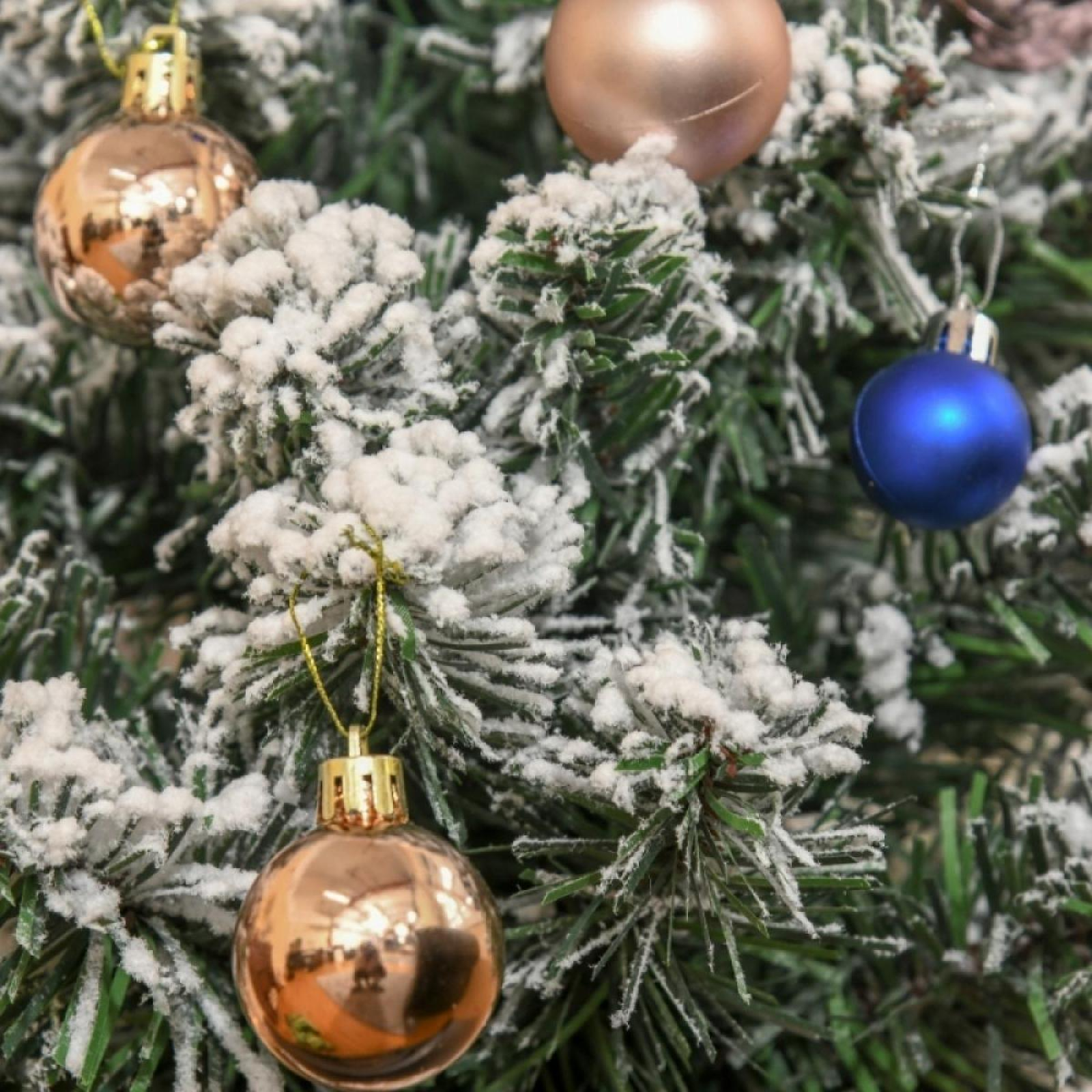 Nahaufnahme eines Weihnachtsbaums mit goldenen und blauen Ornamenten und schneebedeckten Zweigen.