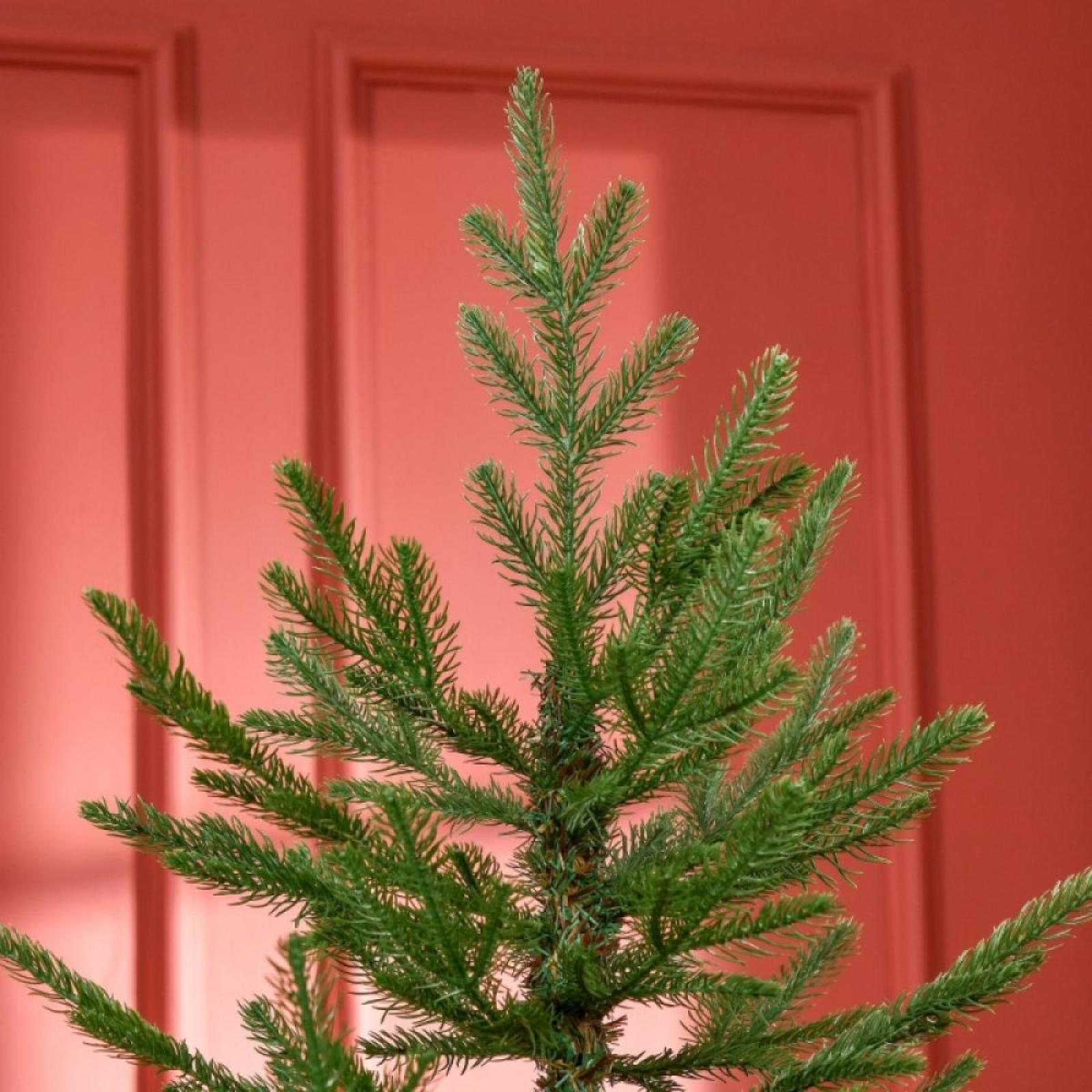 Nahaufnahme eines grünen künstlichen Weihnachtsbaums vor rotem Türhintergrund.