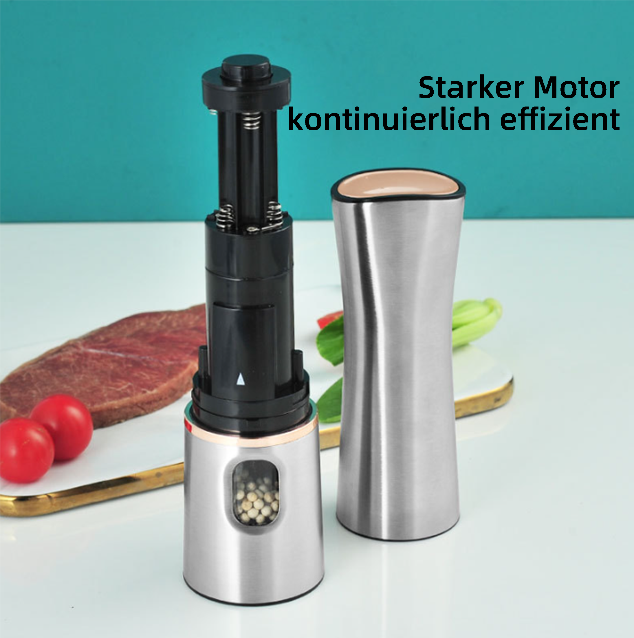 Elektrische Pfeffermühle aus Edelstahl mit Pfefferkörnern, neben einem passenden leeren Behälter. Tomaten und Steak daneben.