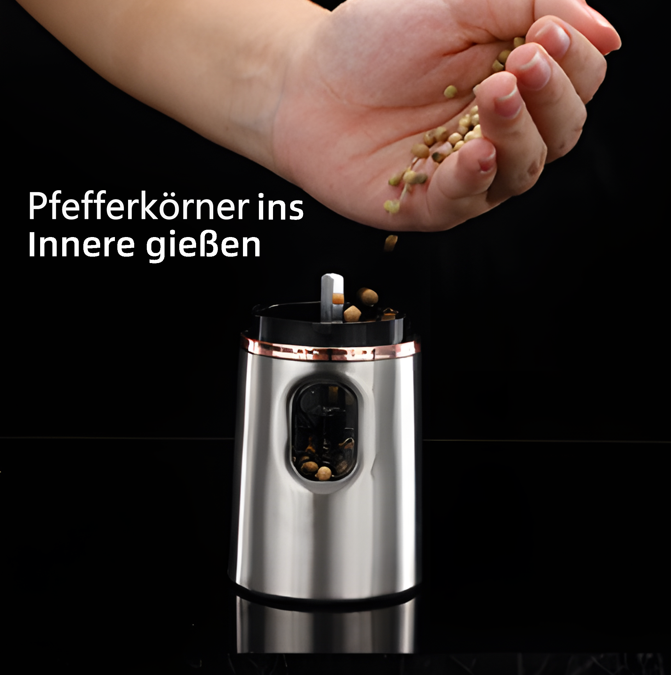 Eine Hand schüttet Pfefferkörner in eine Edelstahlmühle, vor schwarzem Hintergrund.