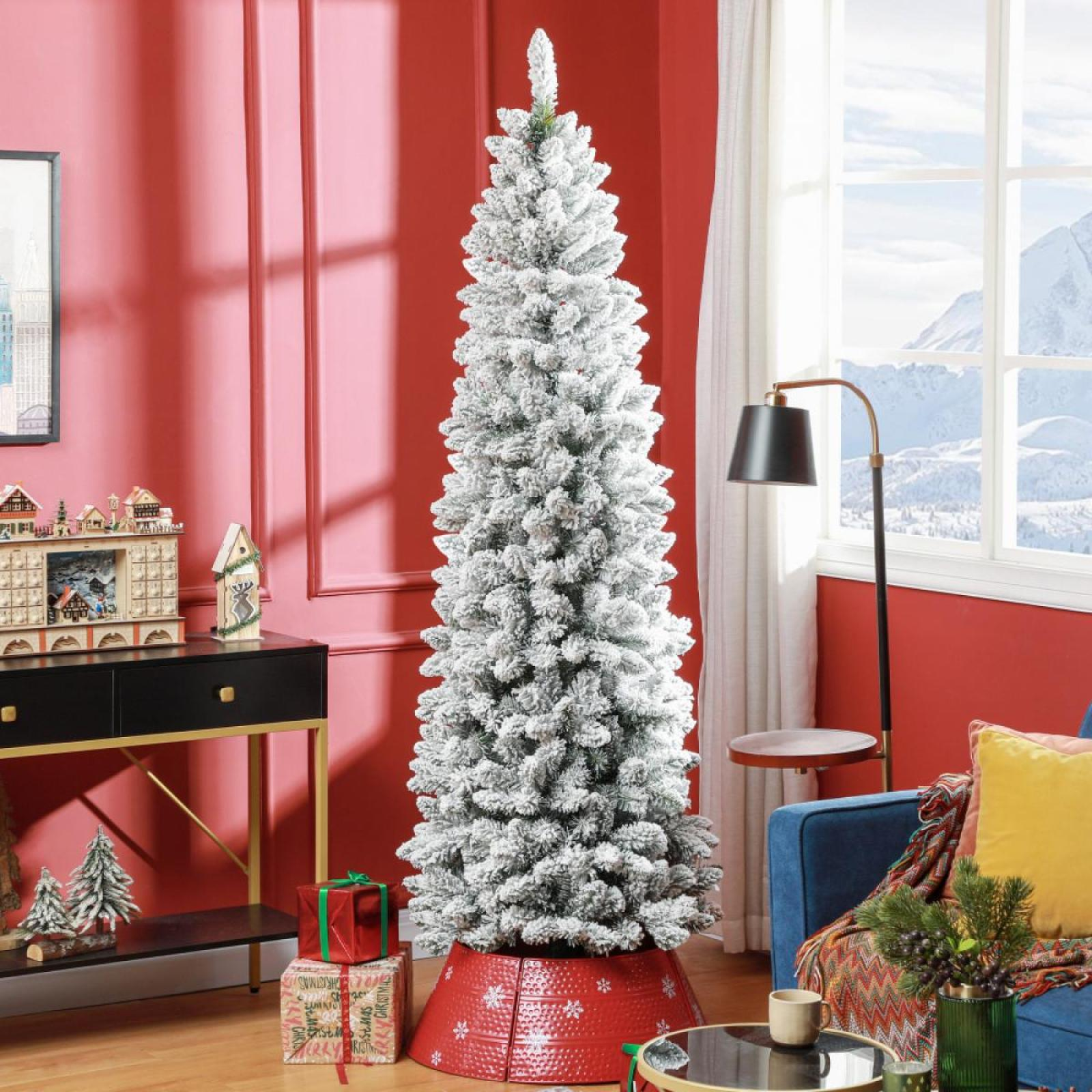 Ein geschmückter Weihnachtsbaum steht in einem rotwandigen Raum mit Geschenken, einer Lampe und einem Fenster mit Blick auf schneebedeckte Berge.
