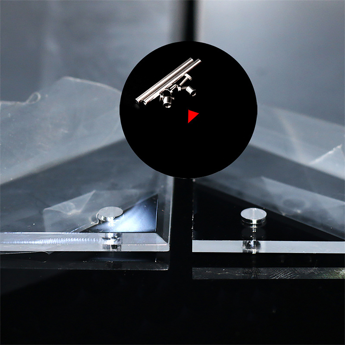 Eine Metallstruktur befindet sich in einem schwarzen Kreis. Klare Glas- und schwarze Glasplatten befinden sich im unteren Teil des Bildes.