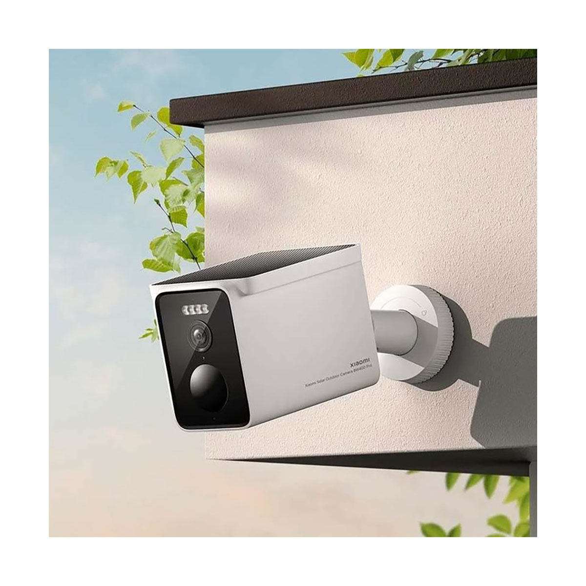 Biała kamera bezpieczeństwa z czarnym obiektywem jest zamontowana na ścianie. Zielone liście i błękitne niebo w tle.