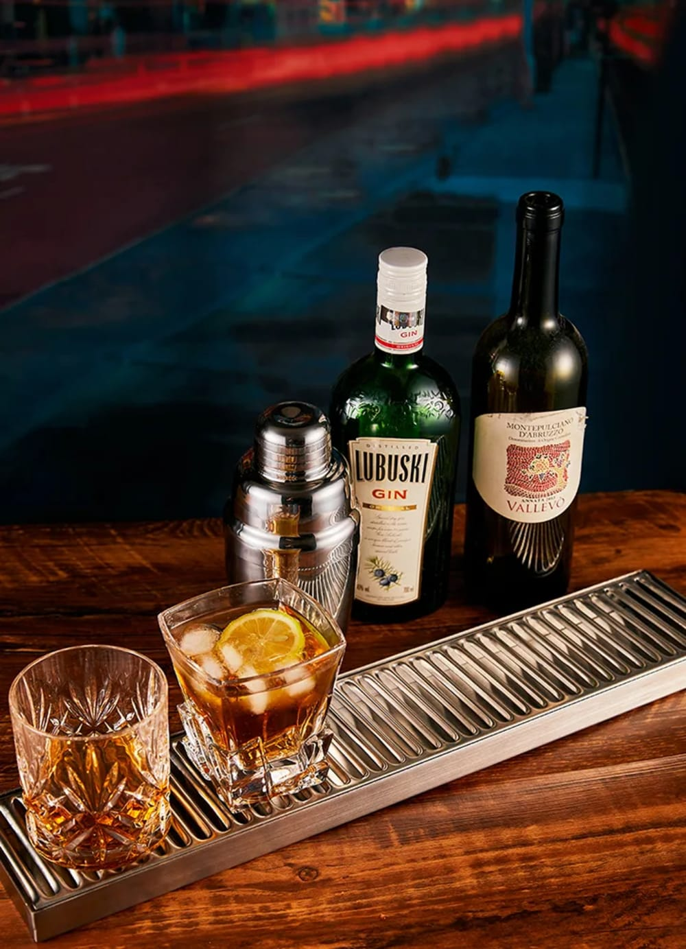 Una scena del bar con gin, vino, un cocktail e uno shaker su una superficie di legno. Una fetta di limone nel cocktail.