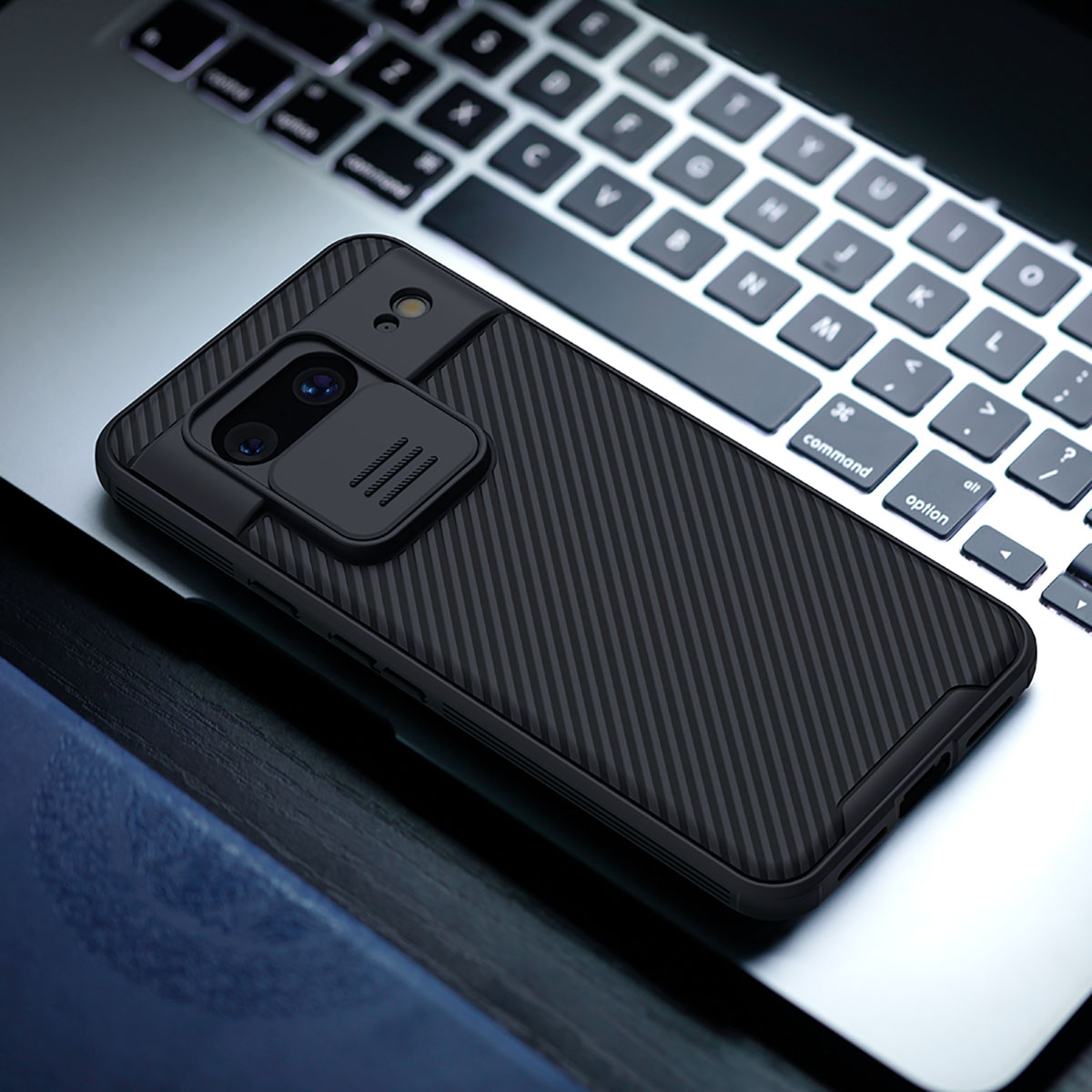 Una custodia nera per telefono con protezione fotocamera è appoggiata su una tastiera di un laptop. La custodia ha un motivo strutturato. Lo sfondo è sfocato.