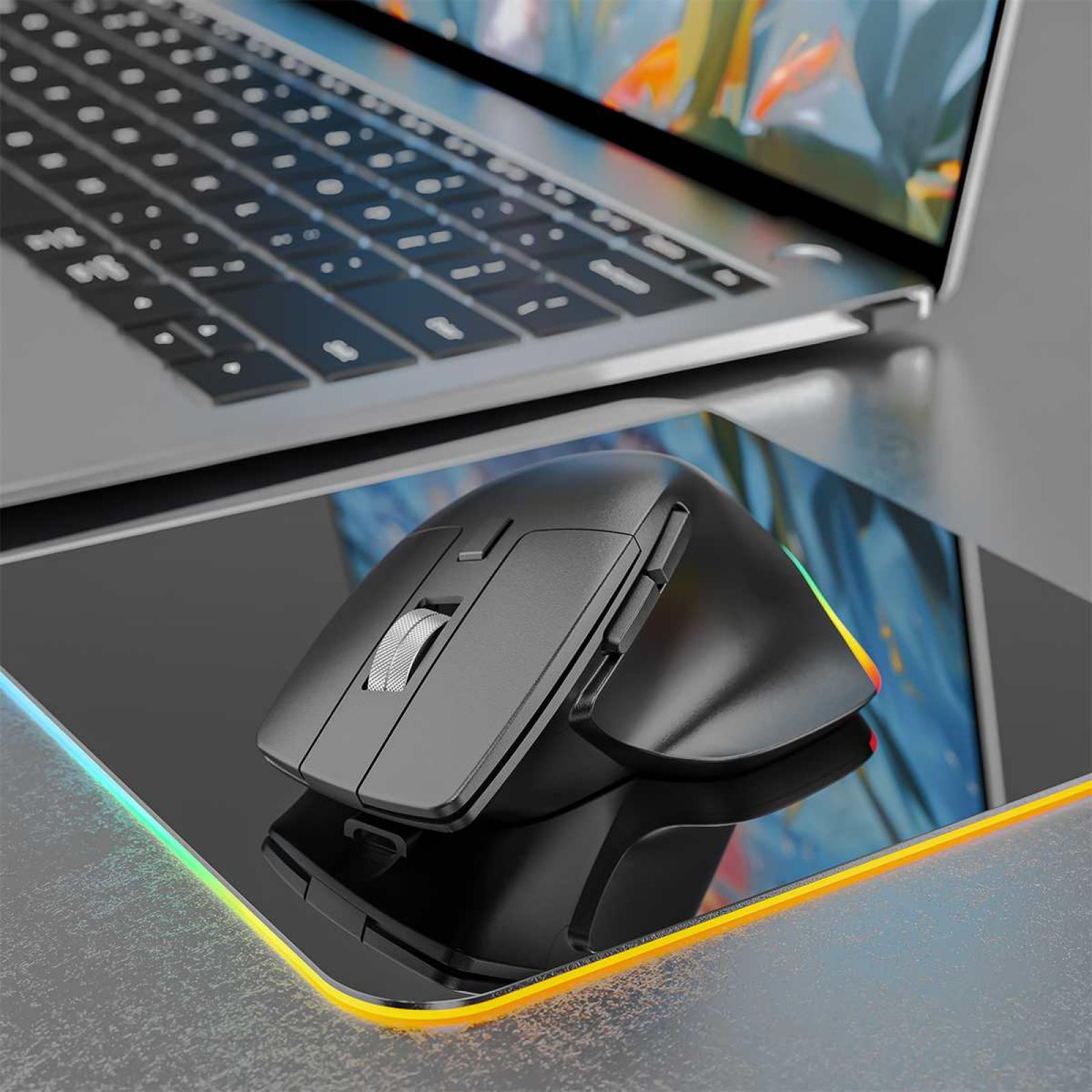 Eine schwarze kabellose Maus liegt auf einem schwarzen Mauspapier mit farbigem Rand, neben einem Laptop.