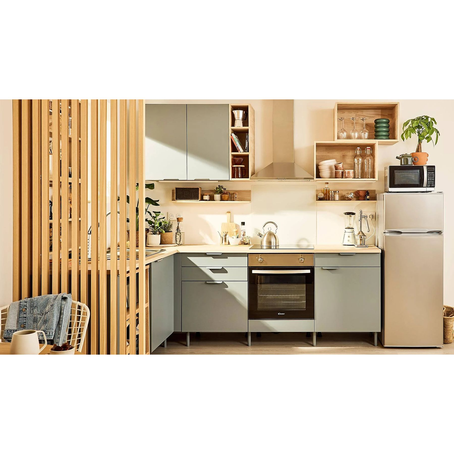 Una cucina moderna con mobili verde chiaro, un divisorio in legno ed elettrodomestici in acciaio inox. Microonde e frigorifero visibili.