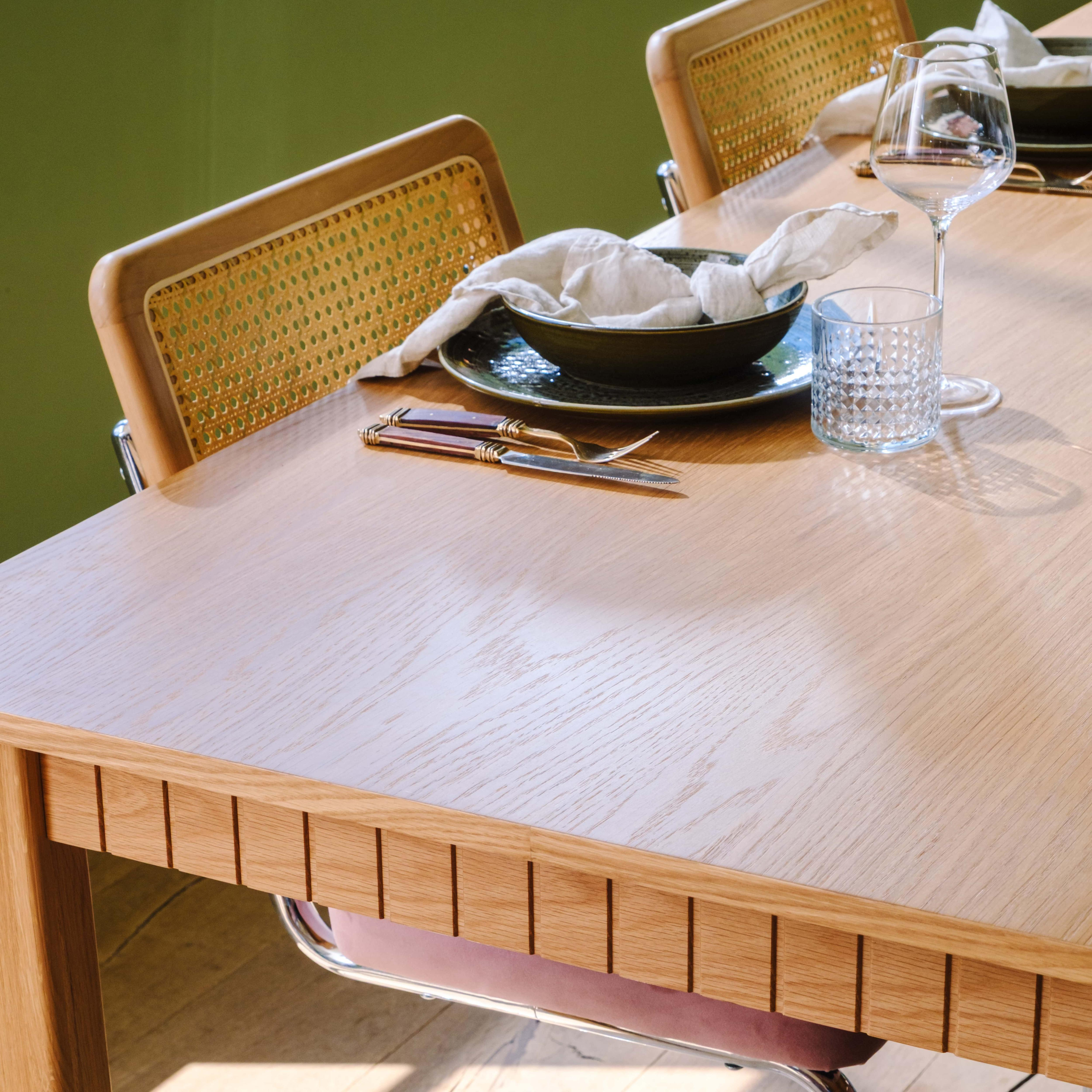 Holztisch mit Teller, Besteck, Glas und LeinenServiette. Zwei Stühle sind im Hintergrund.