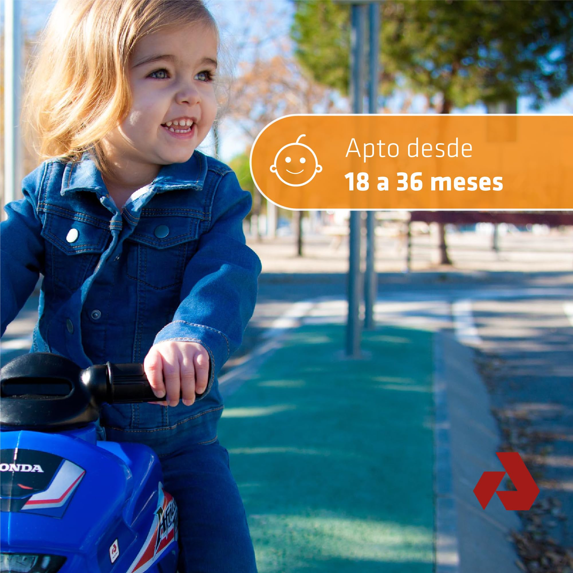 Un niño pequeño sonriendo en una moto de juguete azul. El niño lleva una chaqueta vaquera y está al aire libre. Texto: apto para 18-36 meses.