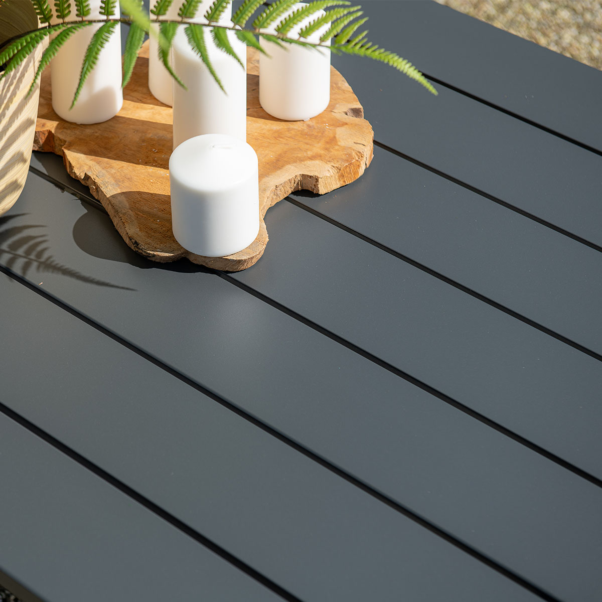 Close-up of a table with candles on a wooden board. Fern leaves and a woven basket are also visible.