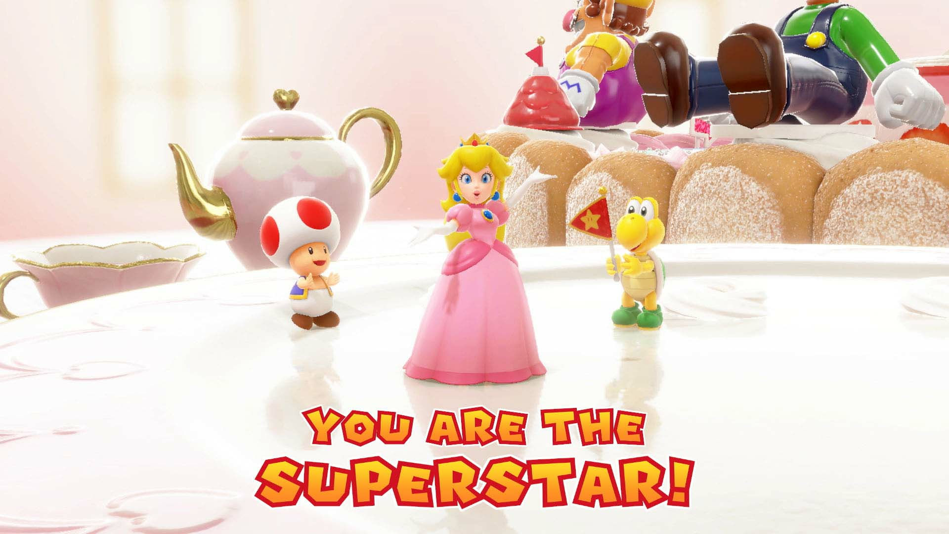La Principessa Peach, Toad e un Koopa Troopa sono su un tavolo. Wario e Luigi sono sullo sfondo. Il testo recita 'You are the Superstar!'