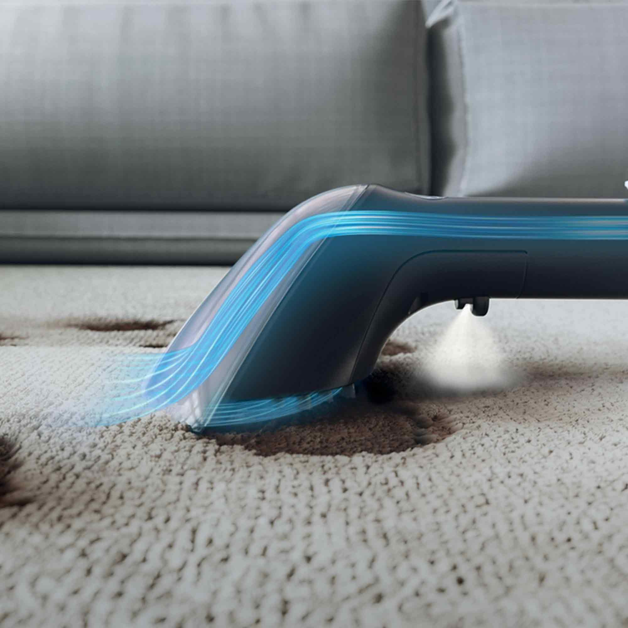 Un pulitore per tappeti spruzza acqua su un tappeto beige. Strisce di luce blu evidenziano il design del pulitore. Sullo sfondo c'è un divano grigio.