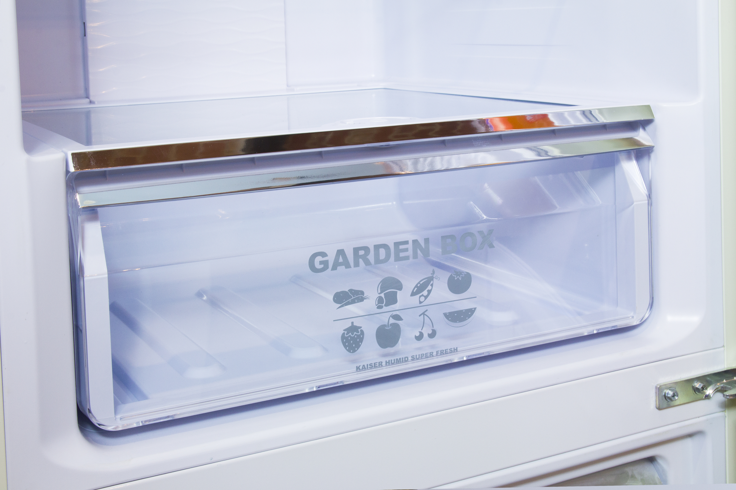 In einem Kühlschrank zeigt eine transparente Schublade mit der Aufschrift 'GARDEN BOX' Obst- und Gemüsesymbole.