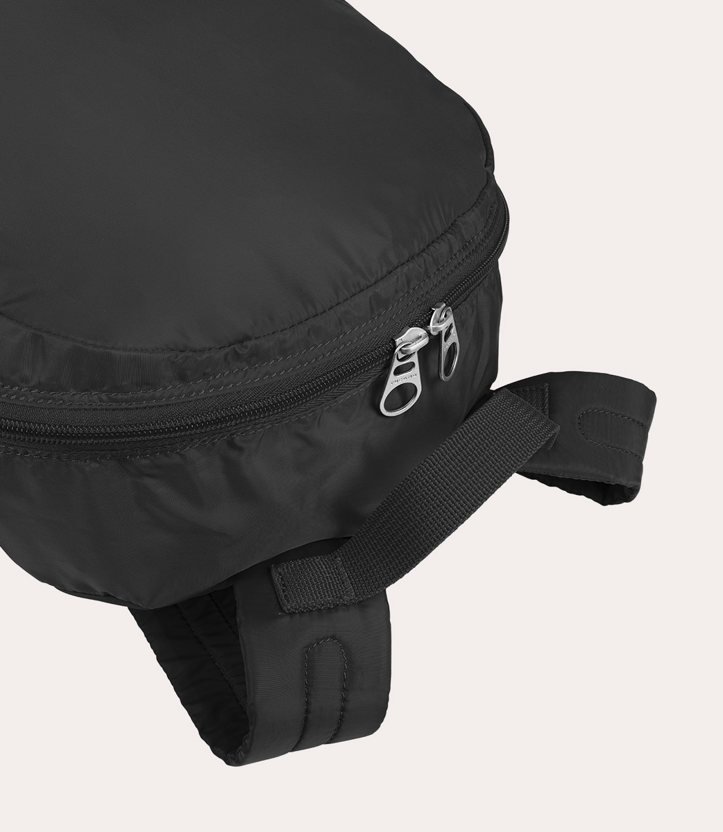 Nahaufnahme einer schwarzen Tasche. Die Tasche hat einen Reißverschluss, einen Riemen und eine gebogene Form. Der Hintergrund ist schlicht.